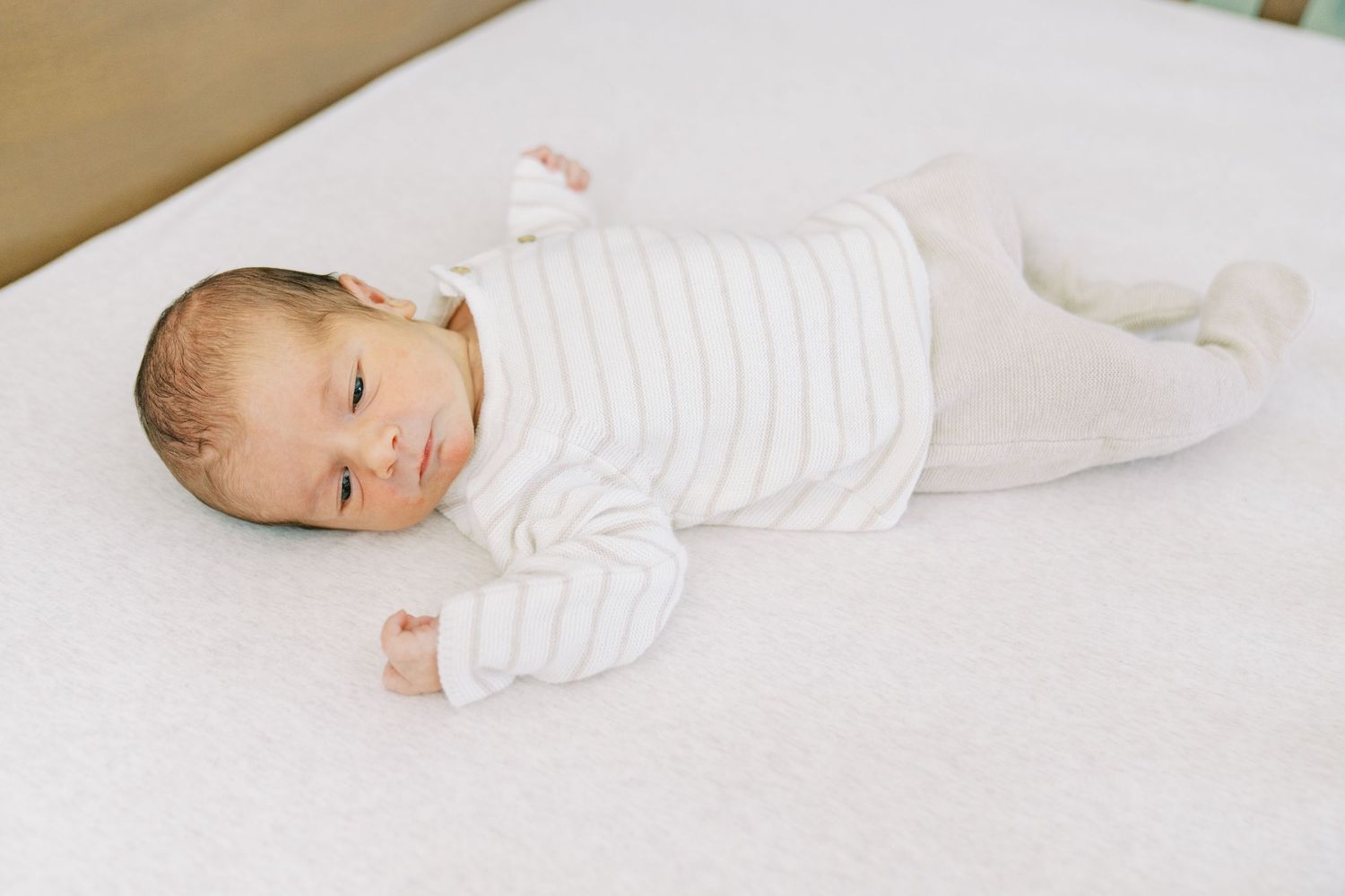 Baby in white clothing lying on soft white bedding in various peaceful resting positions.