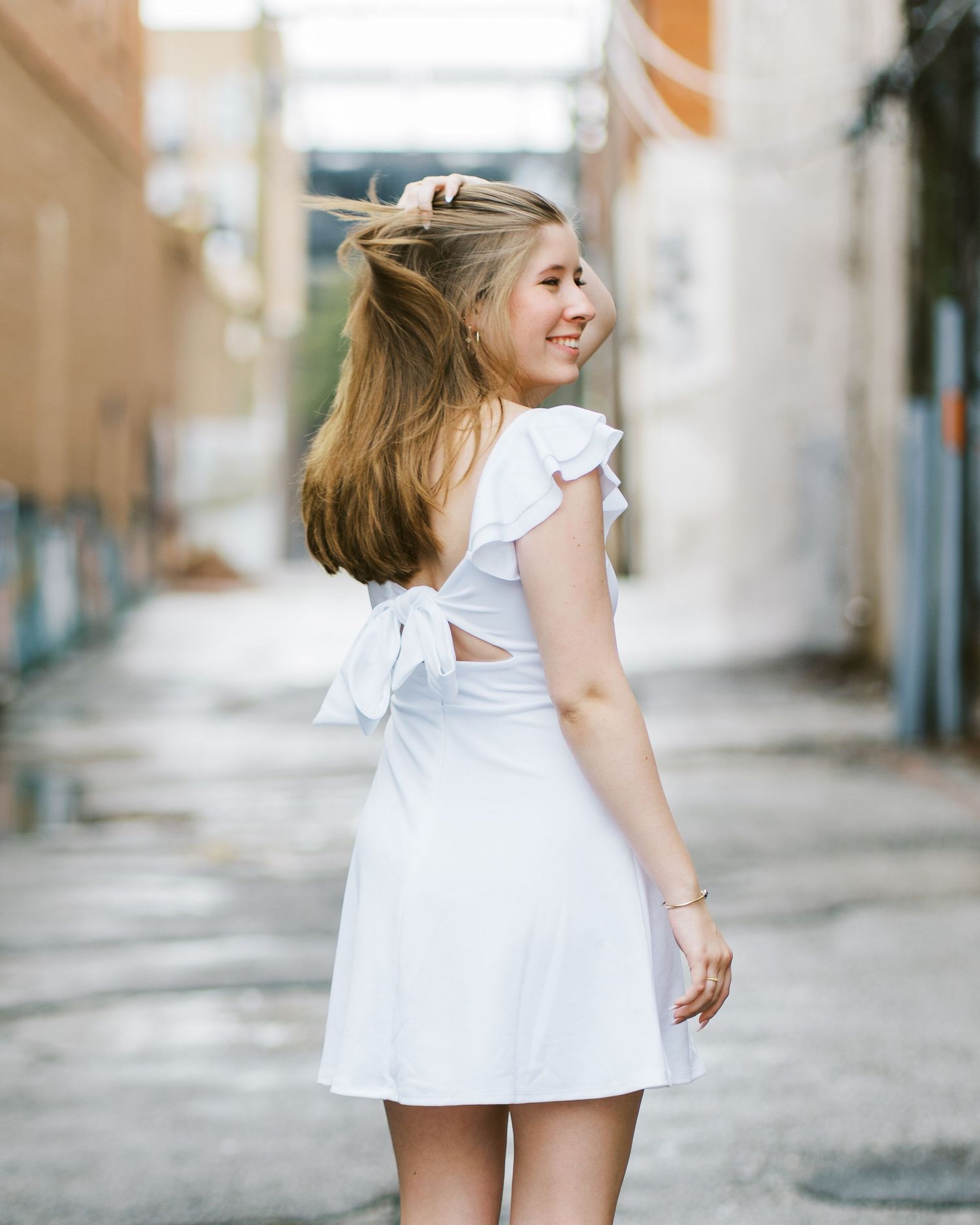 A person in a white dress spins playfully on a cobblestone street in an urban setting.