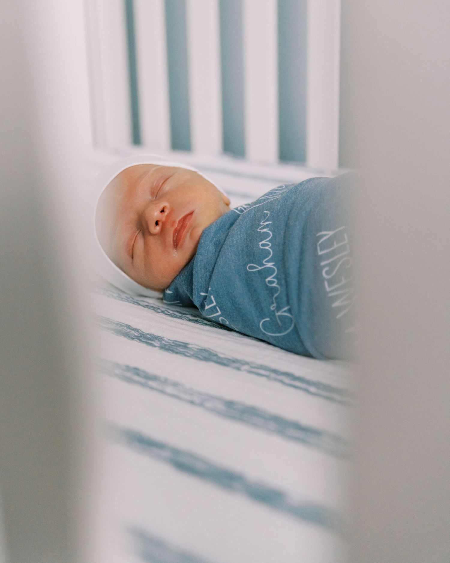 Baby sleeping in crib wearing a blue onesie with white trim.