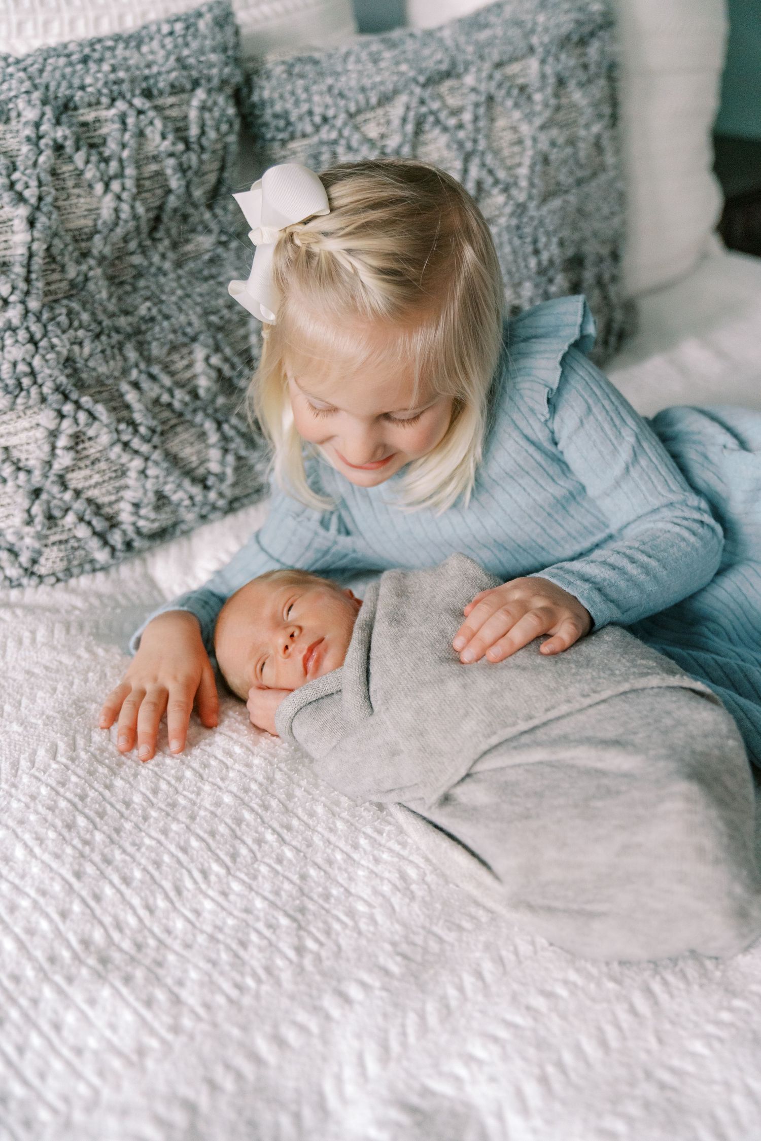 Sweet interaction between siblings on white textured bedding.