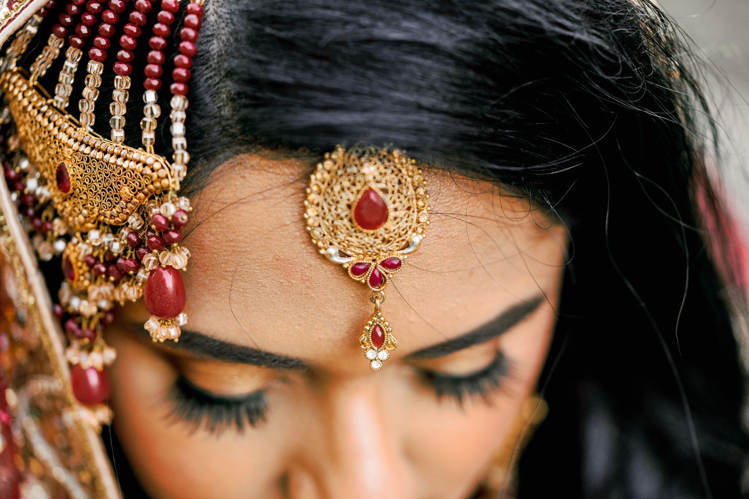 Close-up details of bridal makeup, jewelry and tikka headpiece in traditional Indian style.