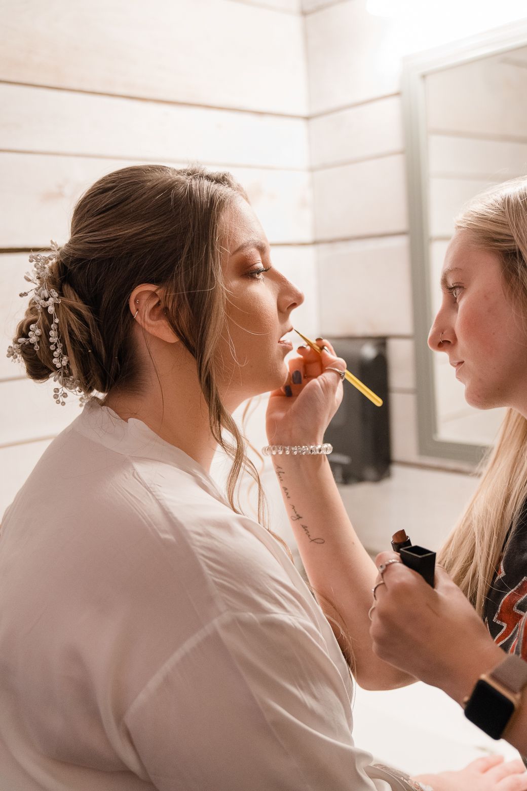 A makeup artist applies cosmetics to a client in a bright white studio setting.