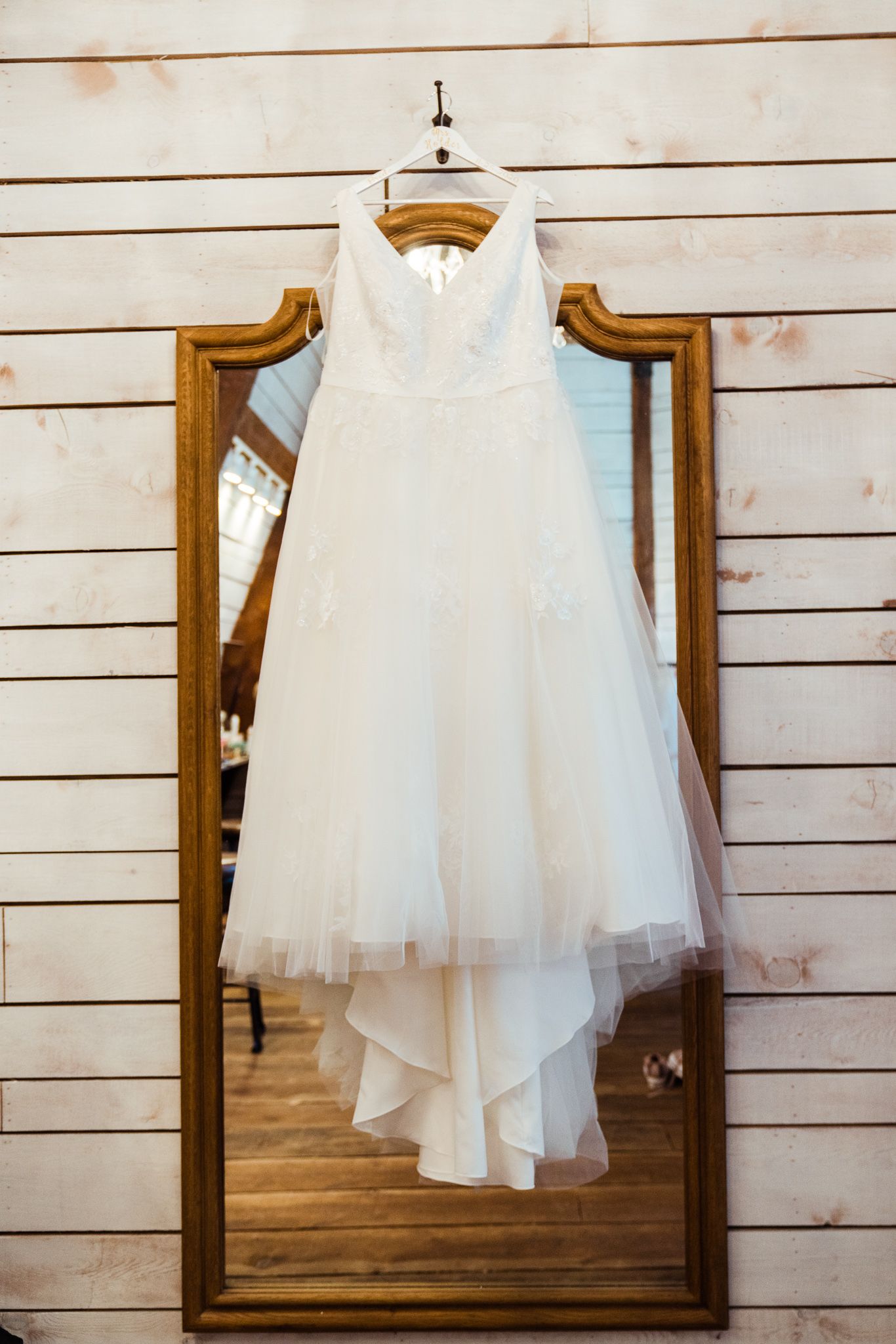 White tulle wedding dress displayed on wooden framed mirrors against shiplap wall.