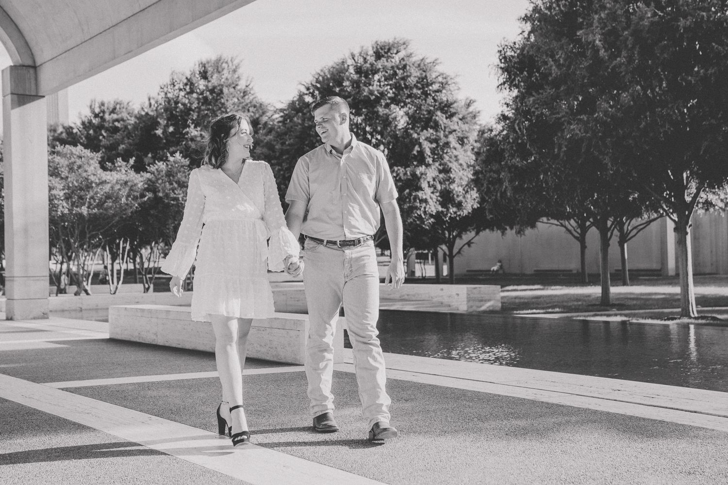 A couple strolls together under a covered walkway in black and white photography.