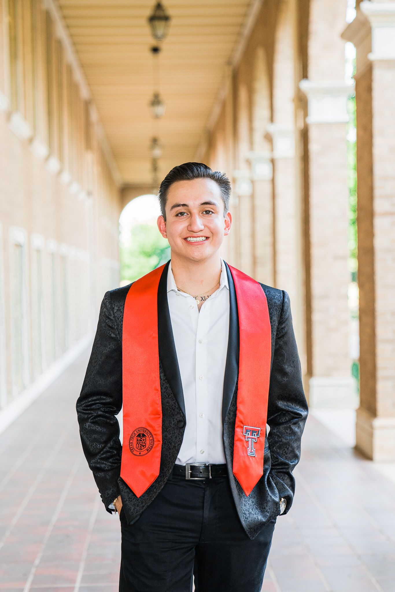 Graduate wearing a black suit and bright red stole poses confidently in a columned hallway.