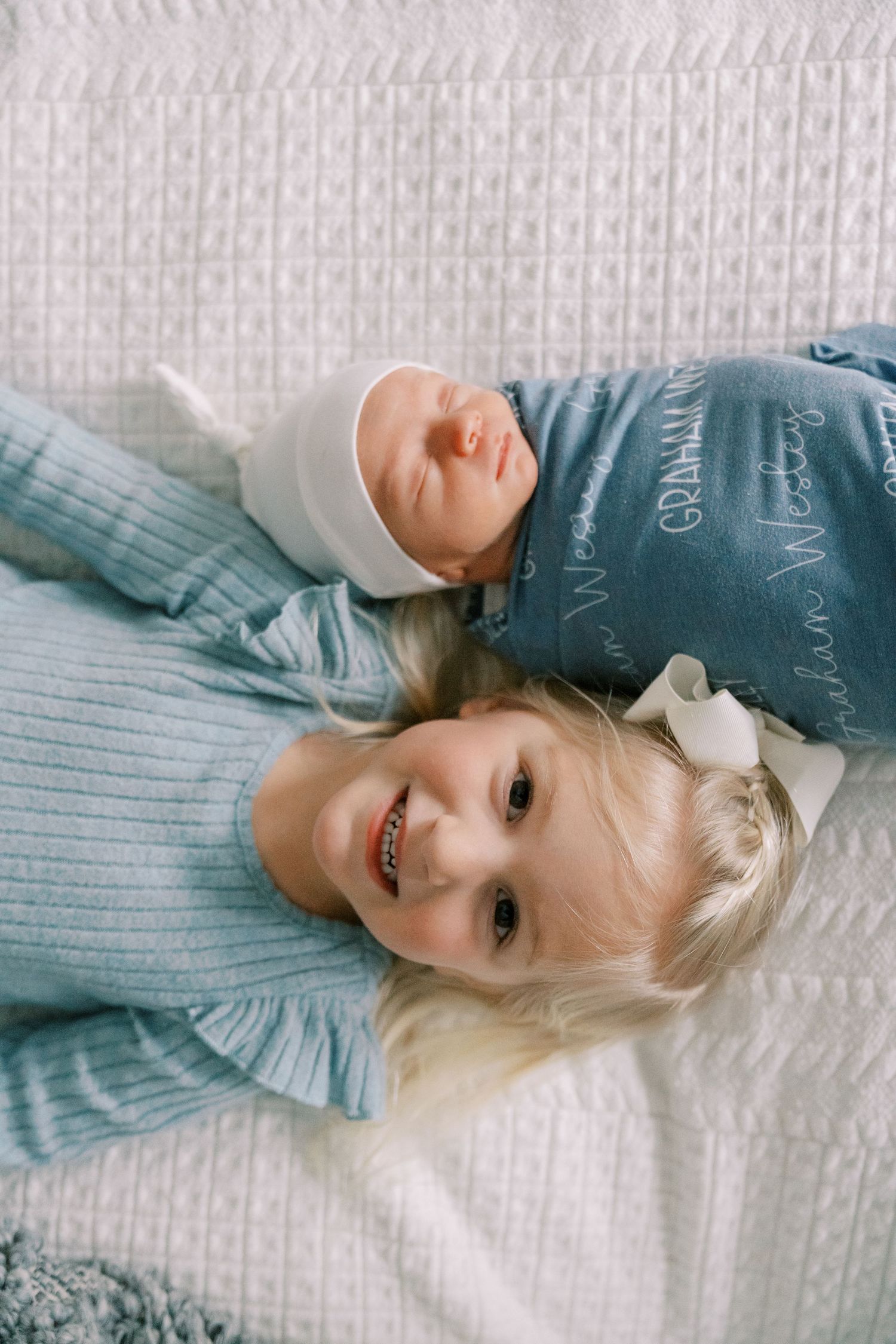 Baby lying on white textured bedding wearing blue and white striped outfit.