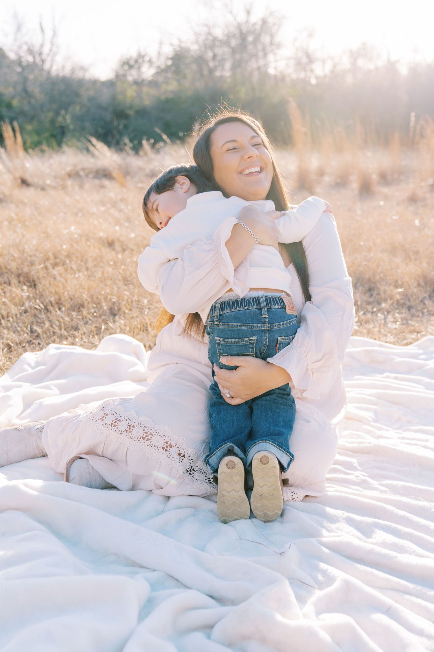 Sweet moments shared on a white blanket in a sun-soaked field during a photo session.