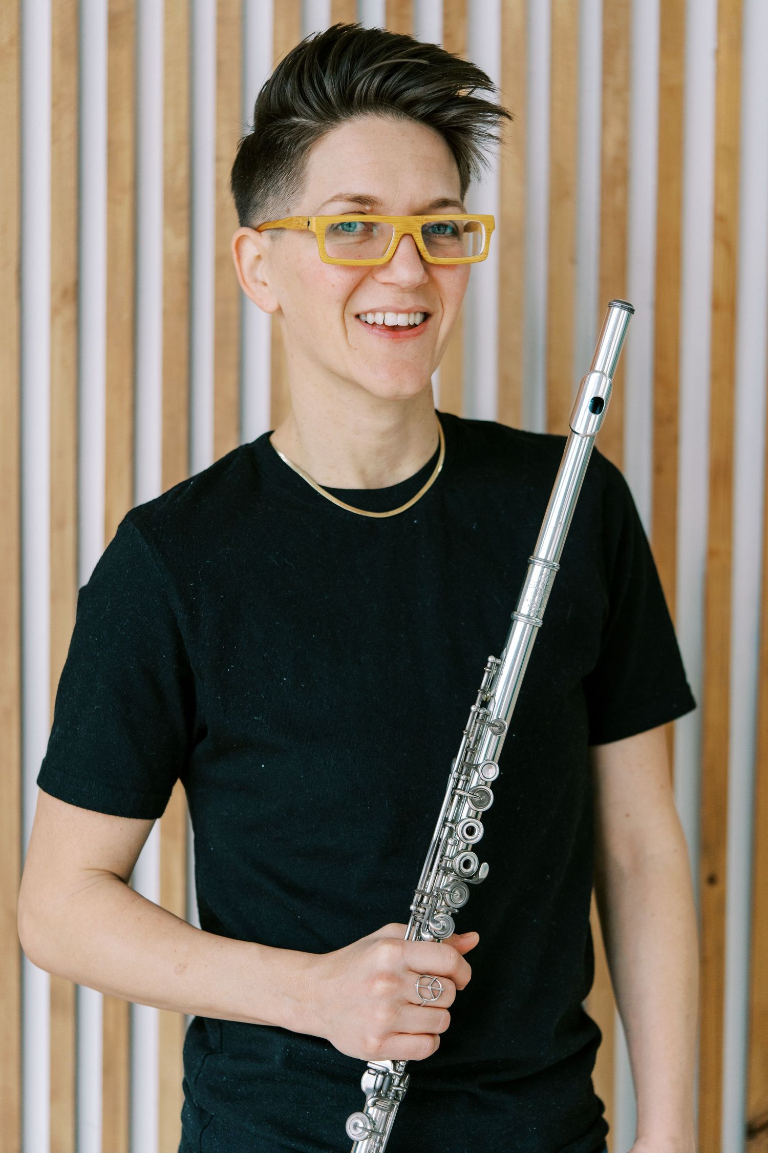 Musician in black t-shirt holding a flute against a striped background, showcasing their instrument.