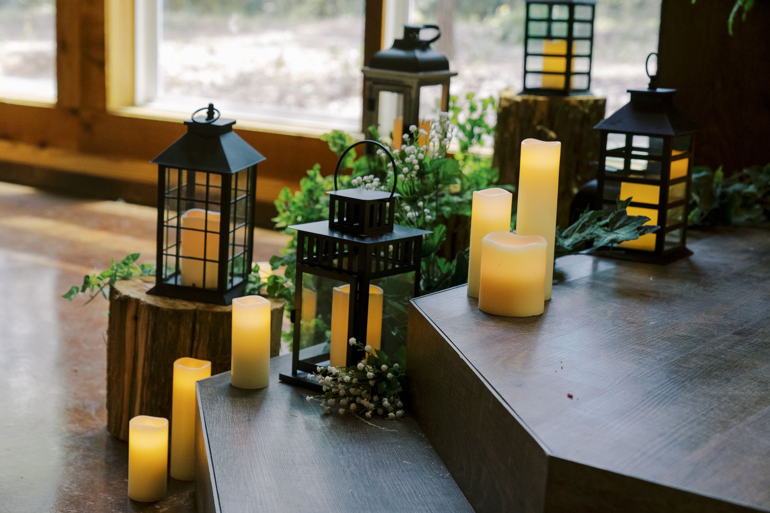Decorative black lanterns and glowing LED candles arranged on wooden platforms with greenery accents create an elegant ambiance.