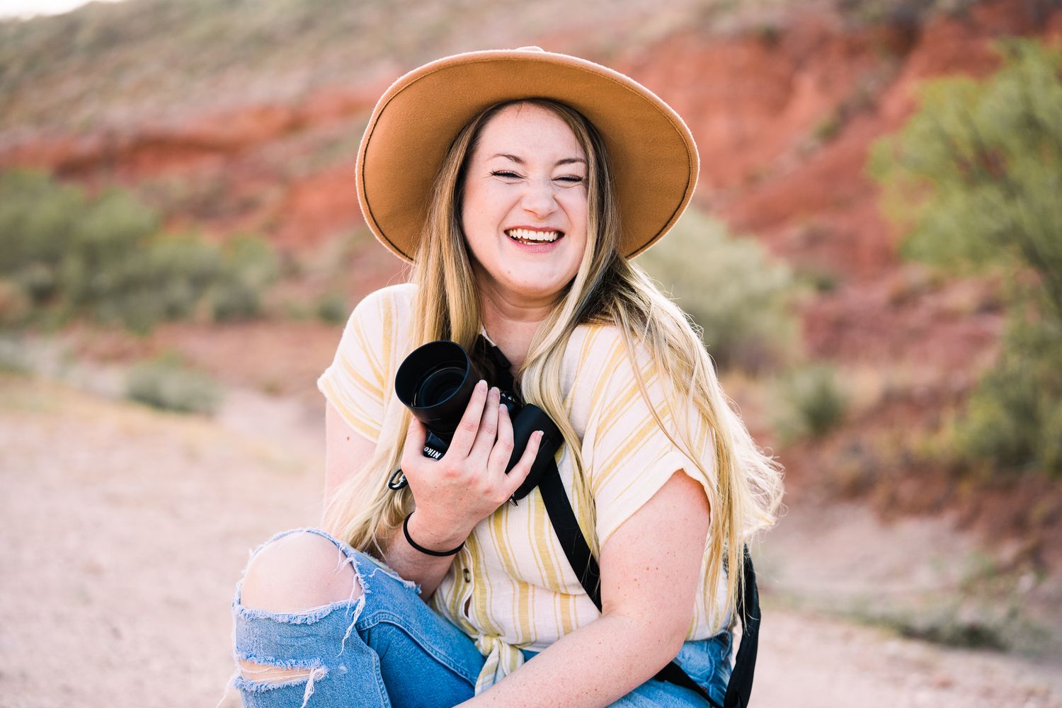 Person in denim and hat laughing joyfully against red rock desert landscape.