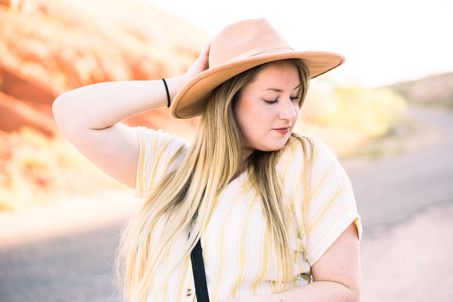 Woman in beige hat and white top with long blonde hair poses outdoors during golden hour.