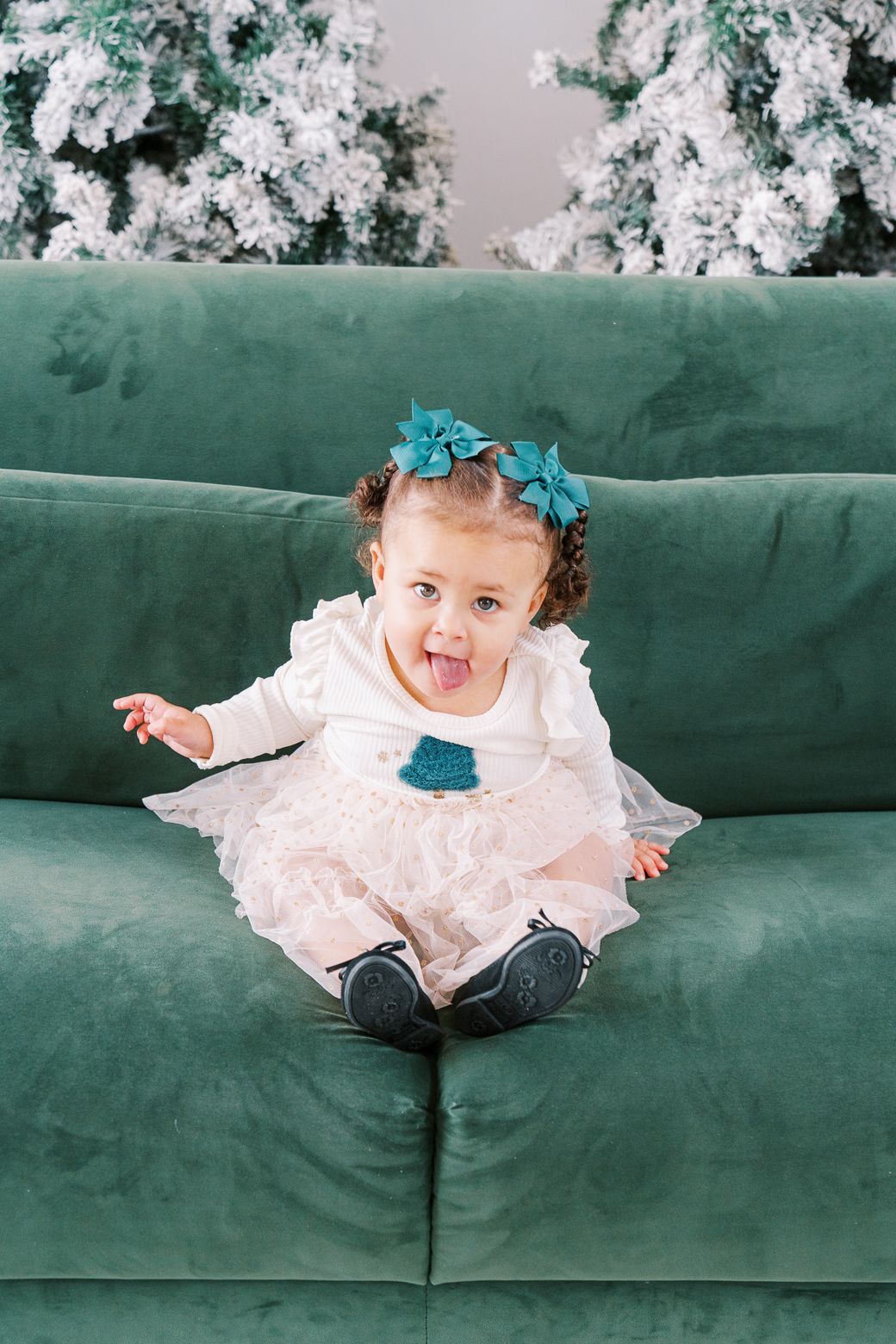 A playful holiday portrait on a plush emerald green couch with snowy Christmas trees as backdrop.