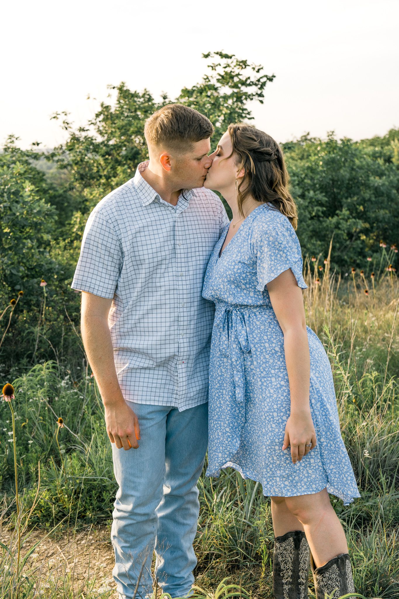 A couple in coordinating blue outfits embrace in a sunny meadow during a romantic photoshoot.