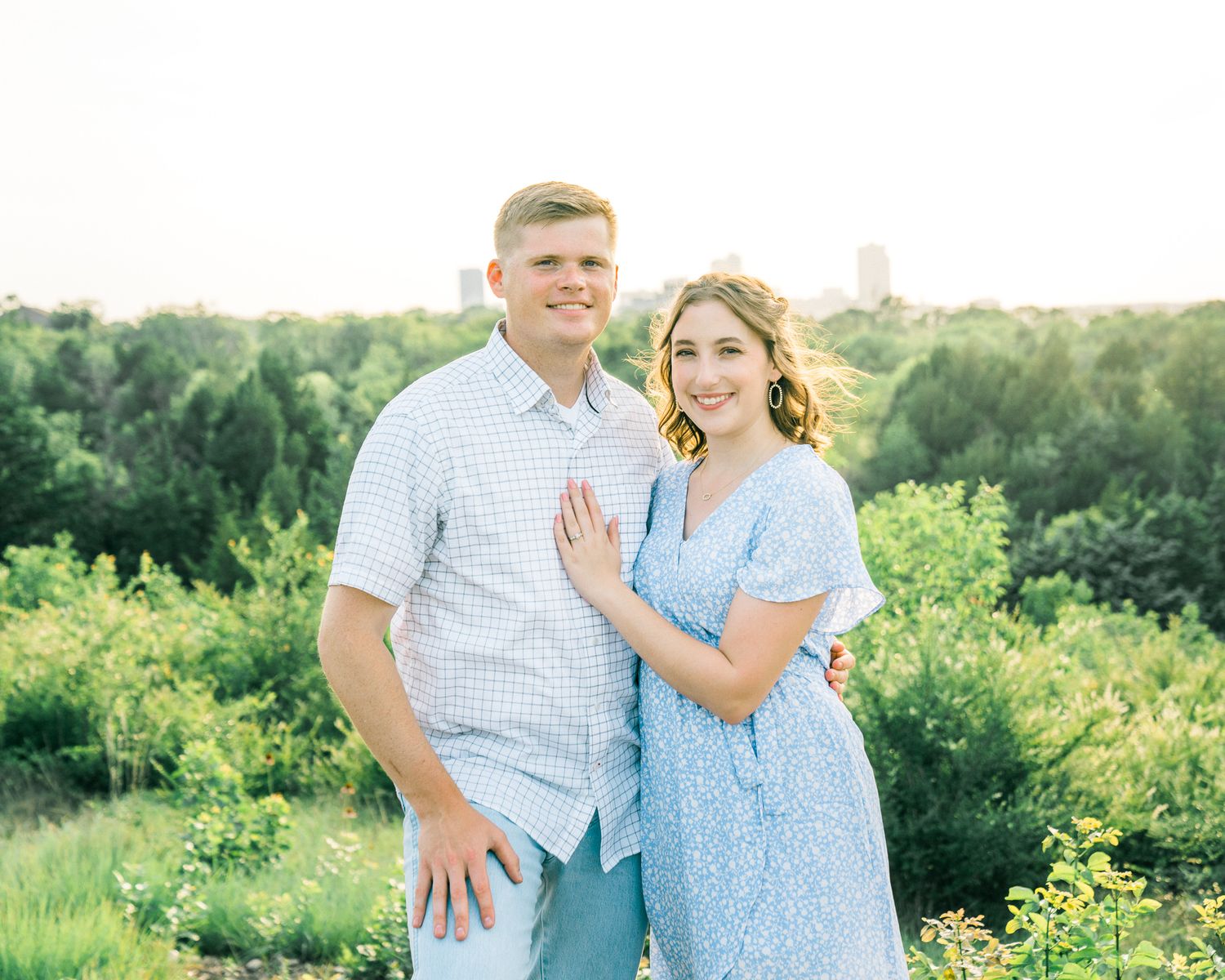 Couple in coordinating blue and white outfits posing together in a lush green summer setting.