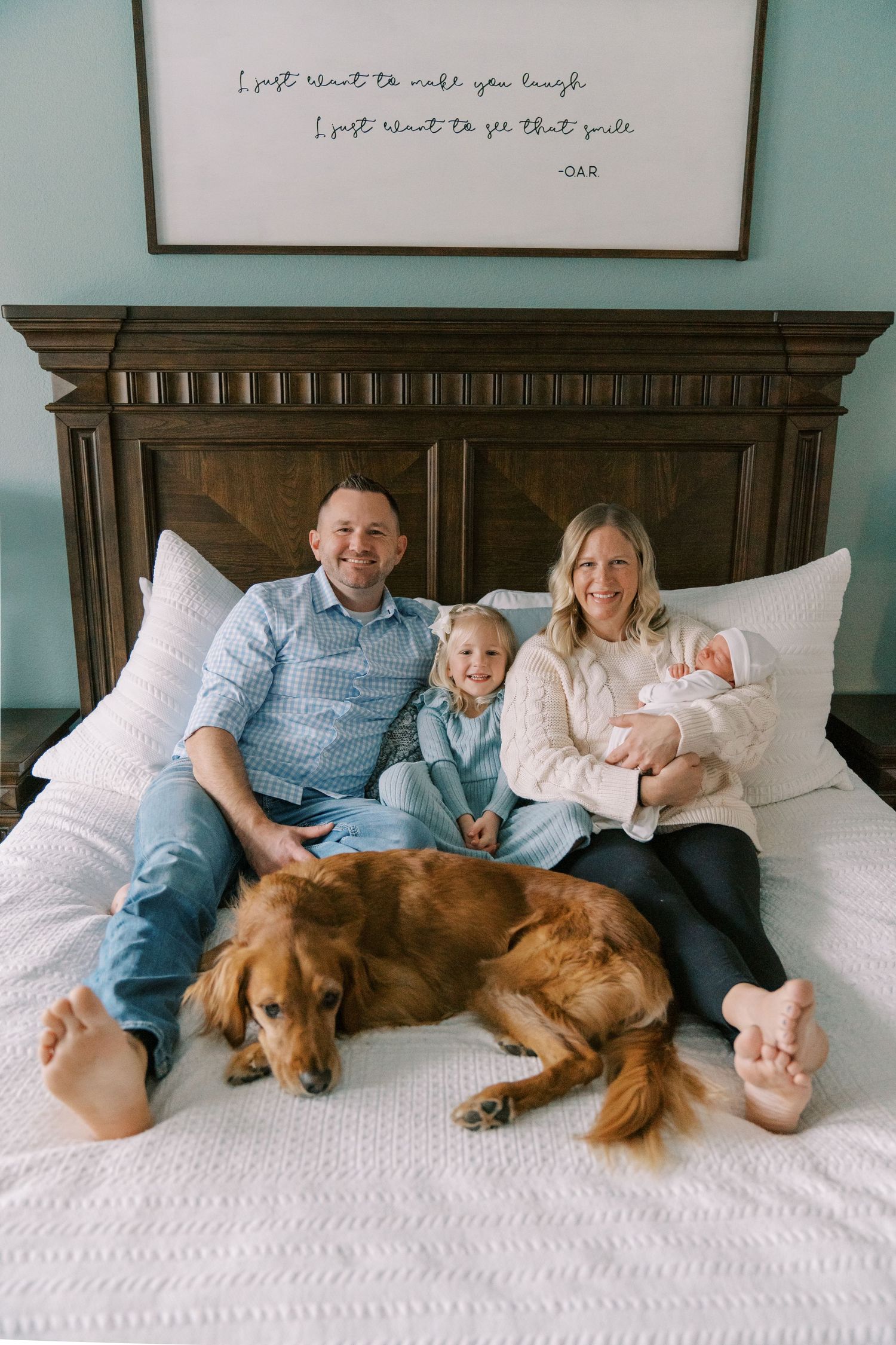 Family and golden retriever dog relaxing together on white bed with blue wall background.