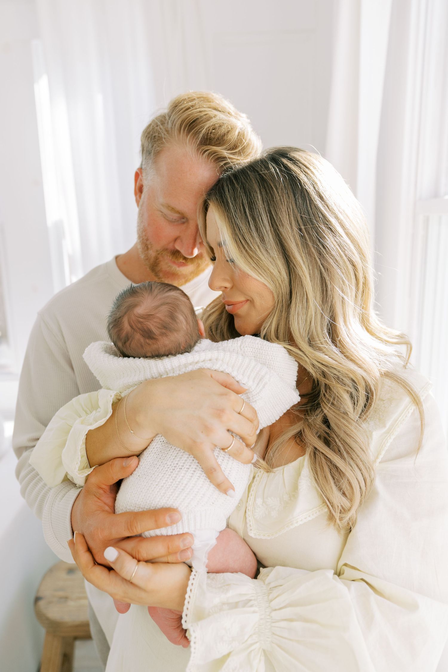Tender family moments captured in white studio photos showing parents embracing their newborn baby.