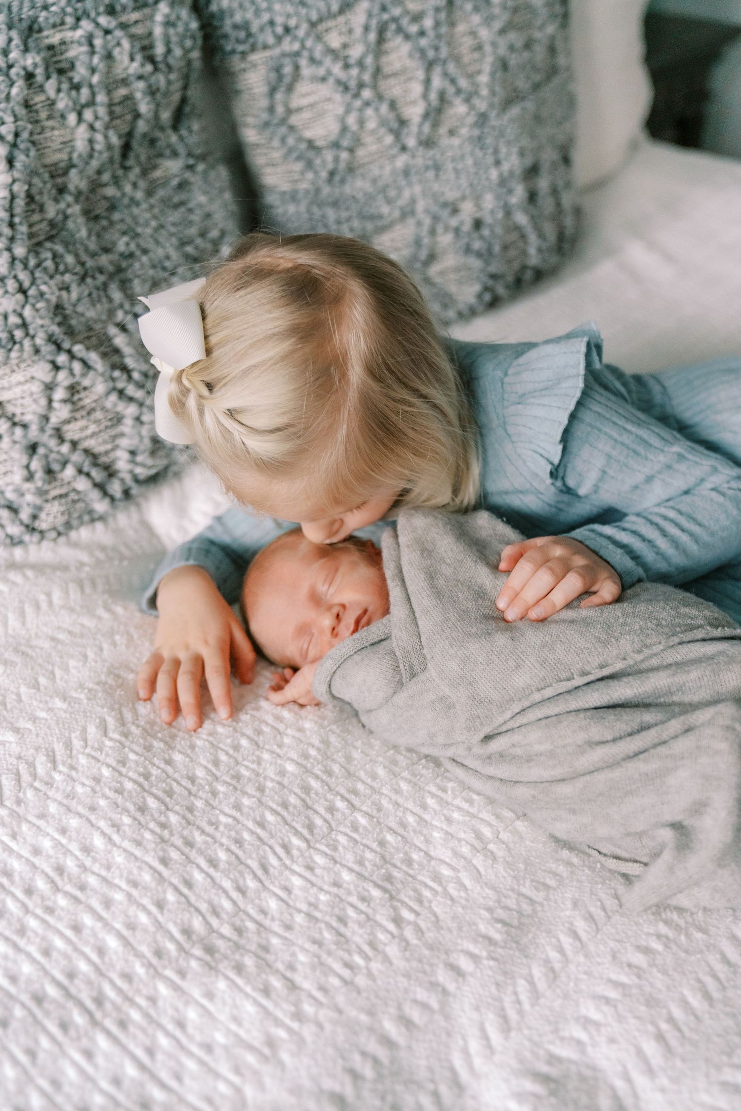 Baby sleeping peacefully on white textured bedding while wrapped in gray swaddle.