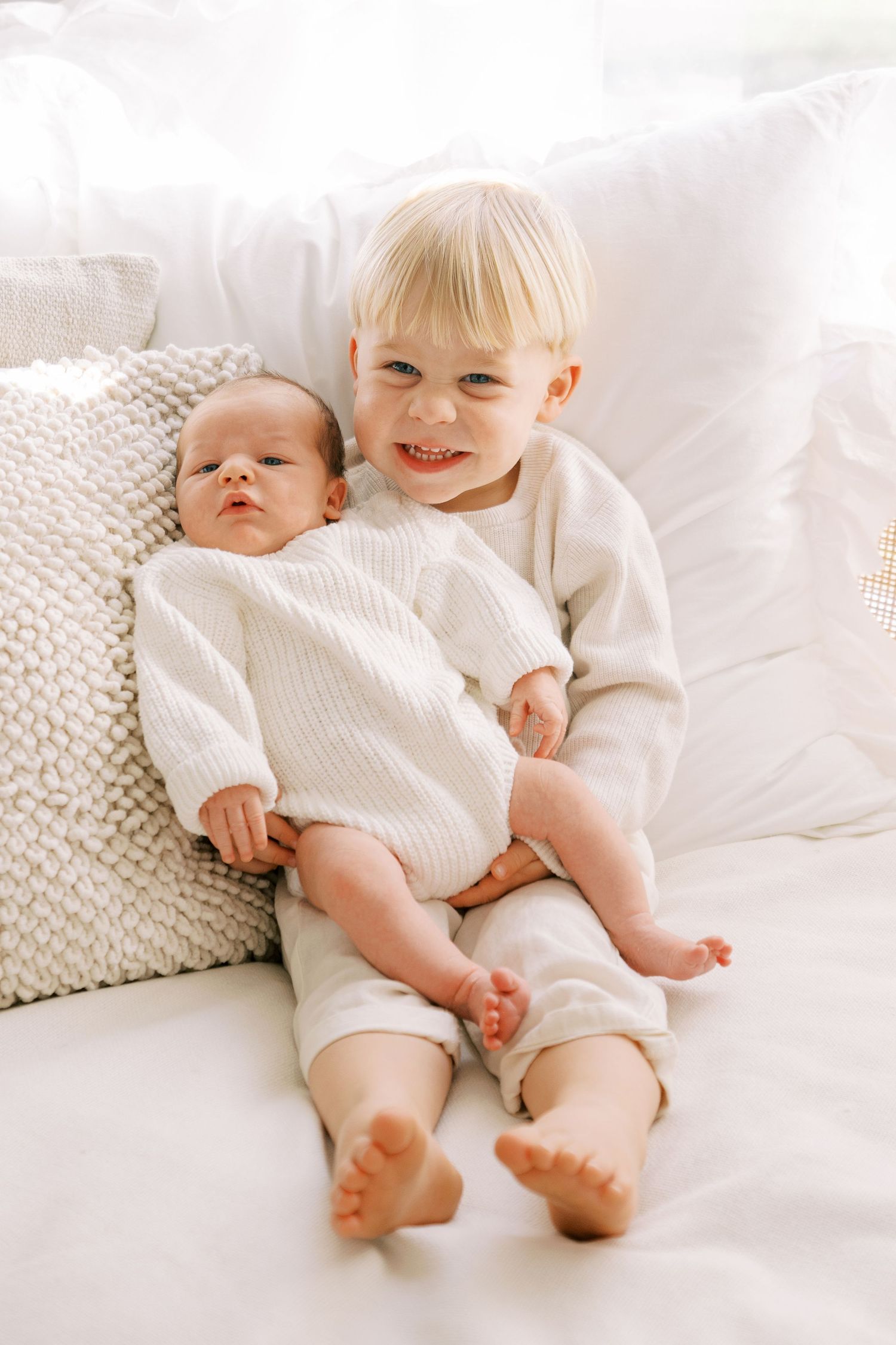 Two young children in white outfits lying on white bedding showing their bare feet.