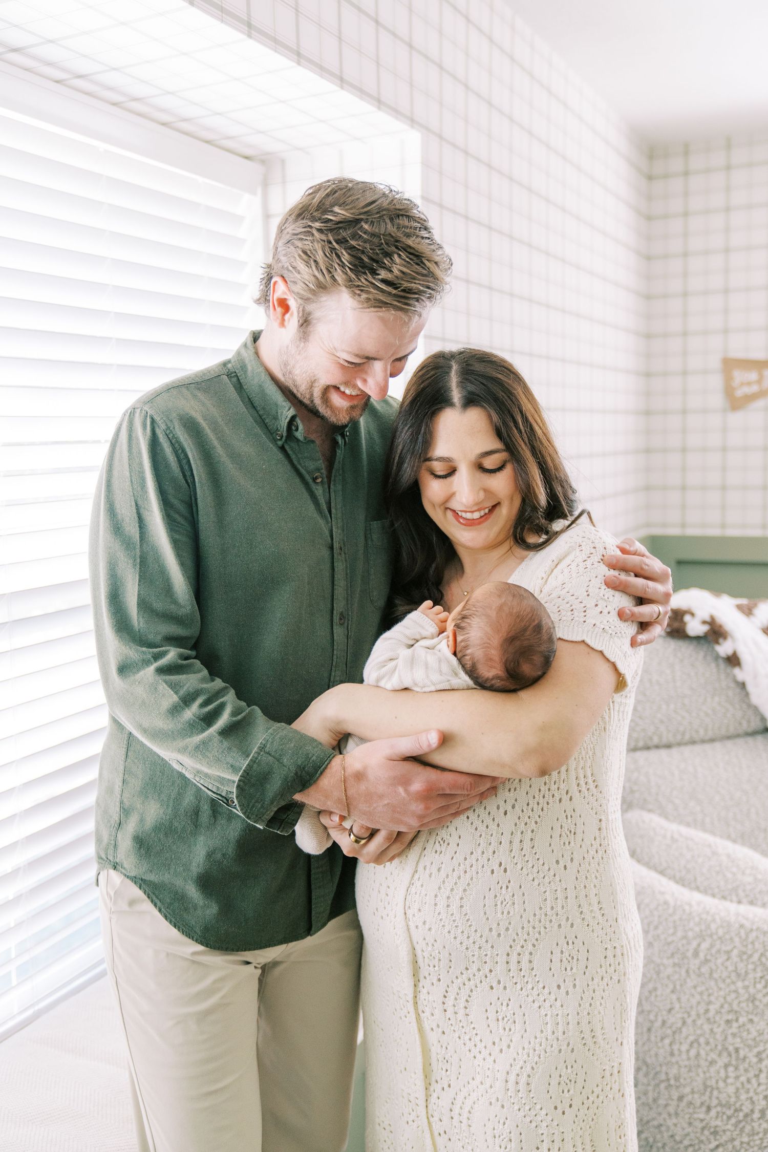 A couple shares tender moments with their newborn baby in a bright white room during an intimate photoshoot.
