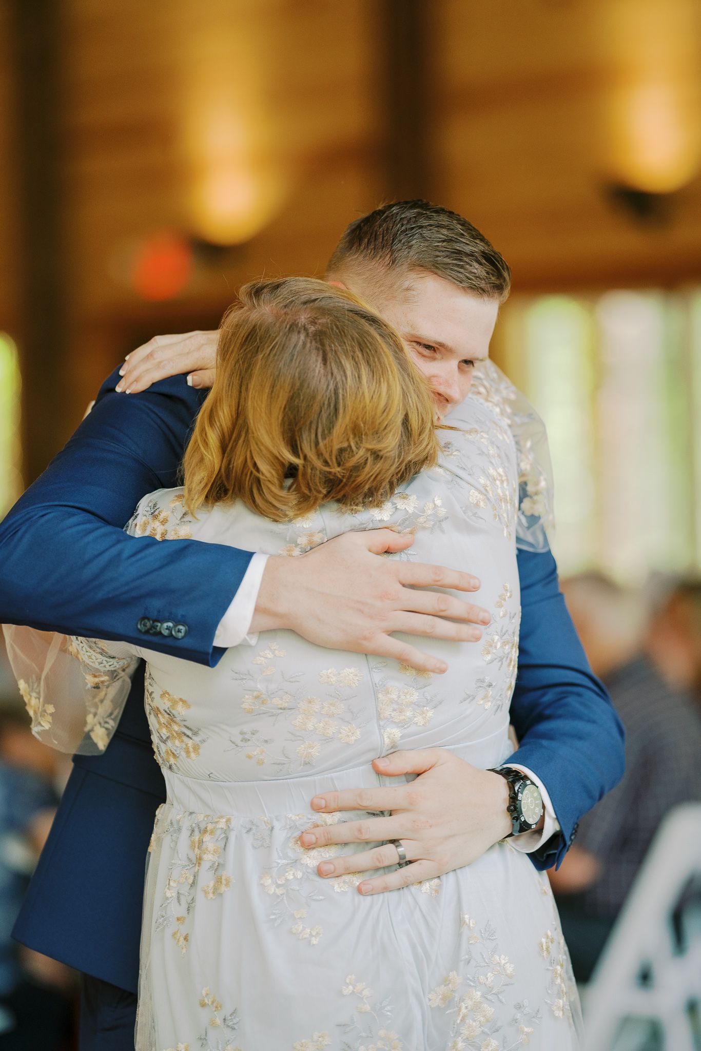 Emotional embrace between two people wearing formal attire at an indoor wedding reception.