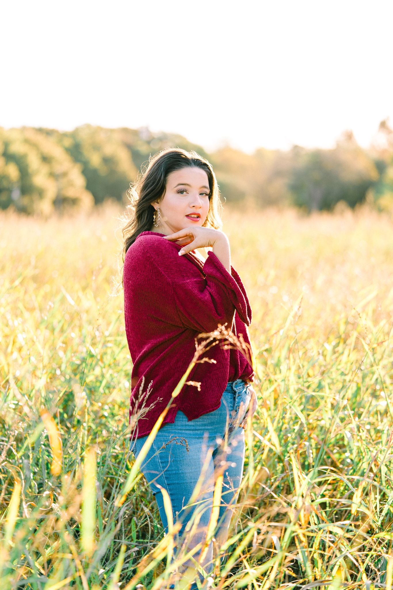 Person in maroon sweater and denim enjoying a carefree moment in a sun-drenched field.