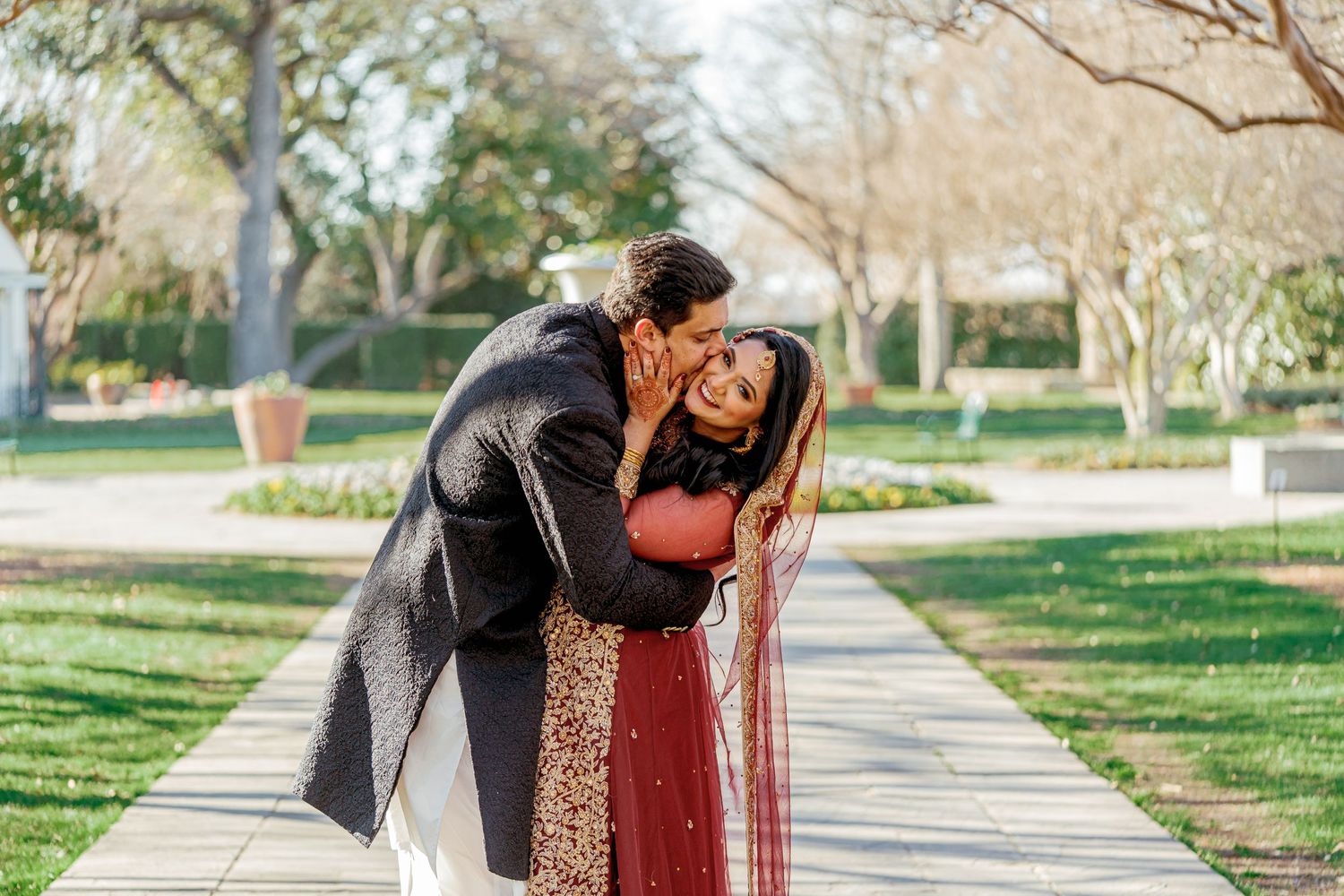 Romantic couple dancing together on a paved pathway surrounded by green grass and trees.
