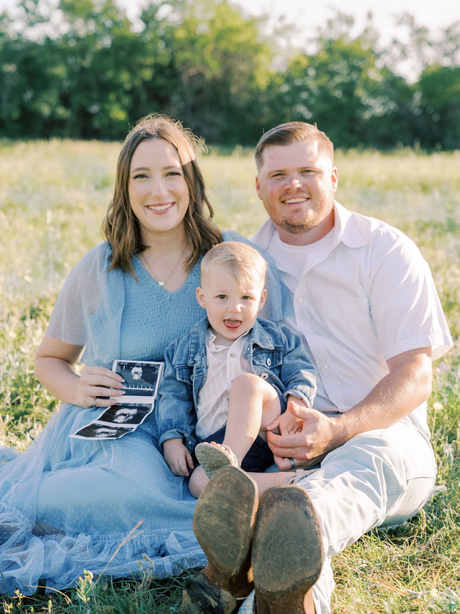 A family sits together in a grassy field during a sunset photoshoot.
