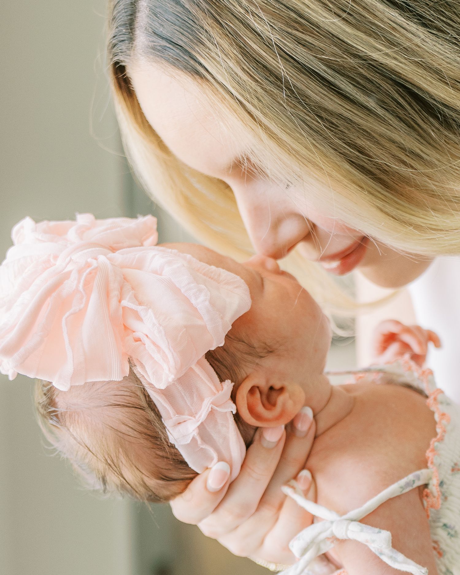 A mother tenderly holds her newborn baby dressed in a pink ruffled outfit, gently touching foreheads in an intimate moment.