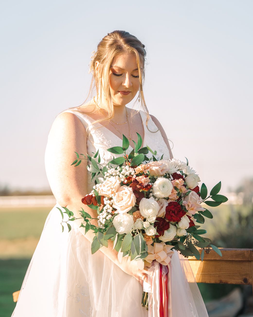Elegant bridal bouquet featuring blush pink and deep red roses with cascading silk ribbons against a dreamy sunset backdrop.