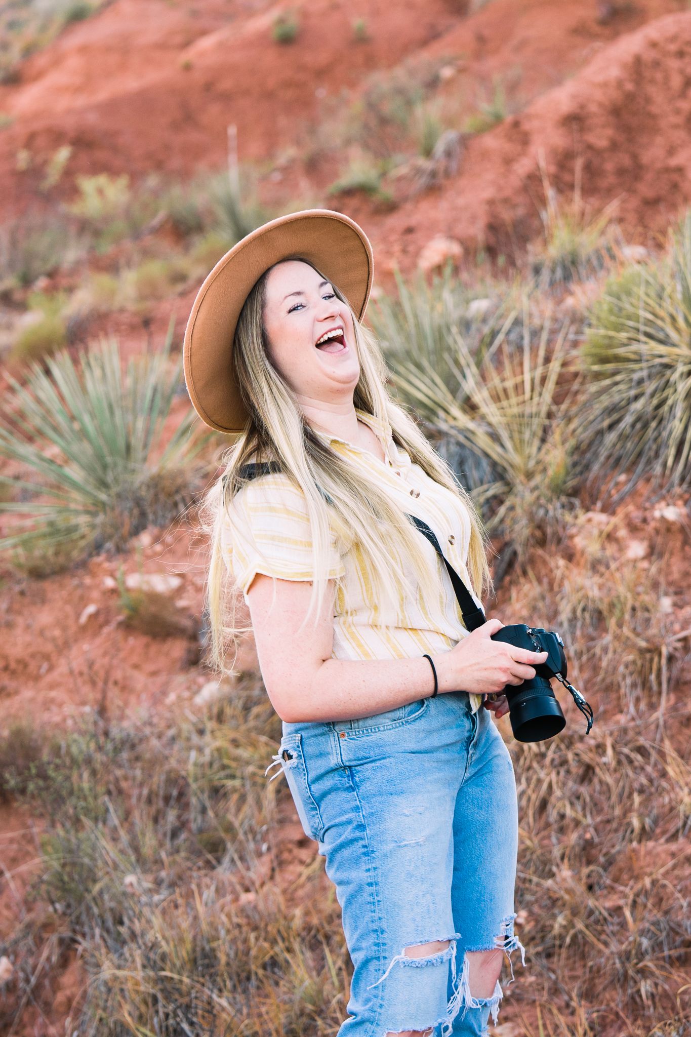 Candid photography session in front of vibrant red rocks with a person in casual denim and a sun hat.