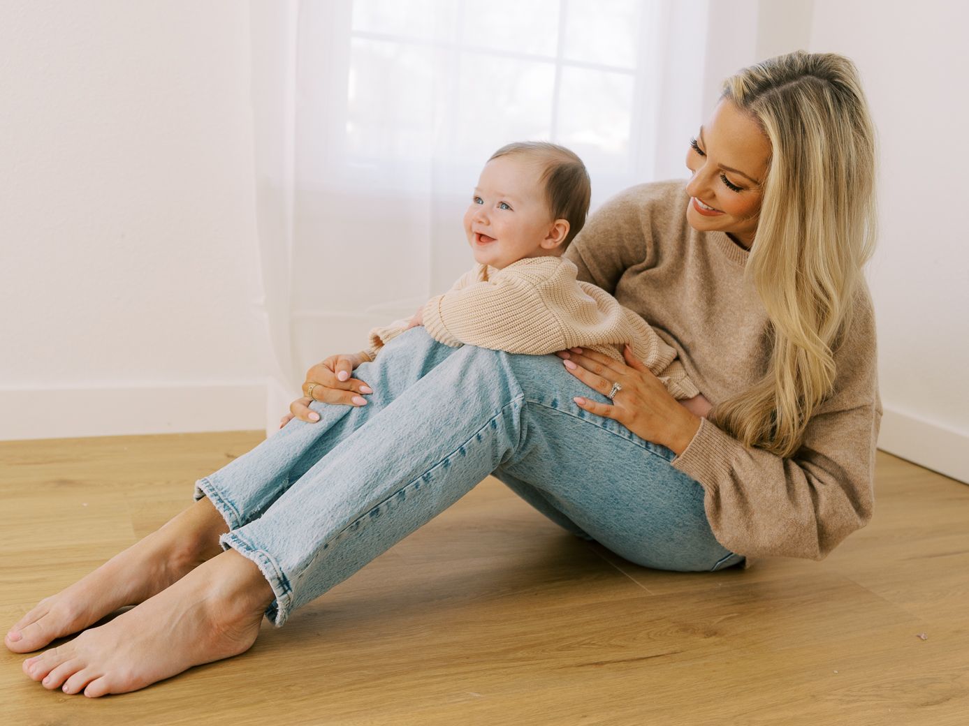 Parent and baby sharing tender playful moments together on light wooden floor.