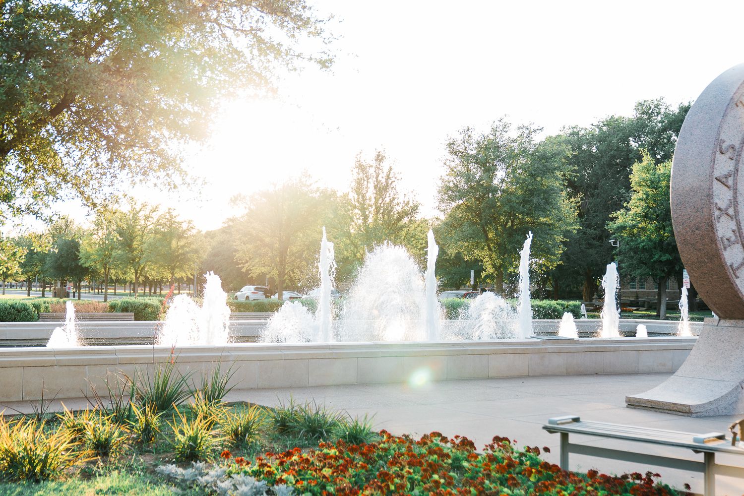 Beautiful fountain display with water jets in a landscaped garden park at sunset with colorful flowers in the foreground.