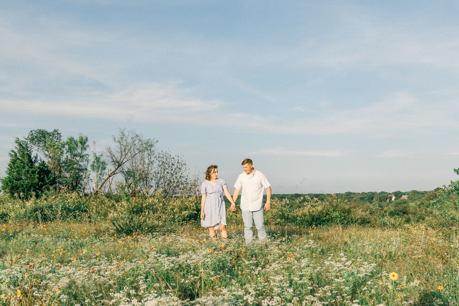 A couple walks through a scenic wildflower meadow on a sunny summer day against a blue sky.