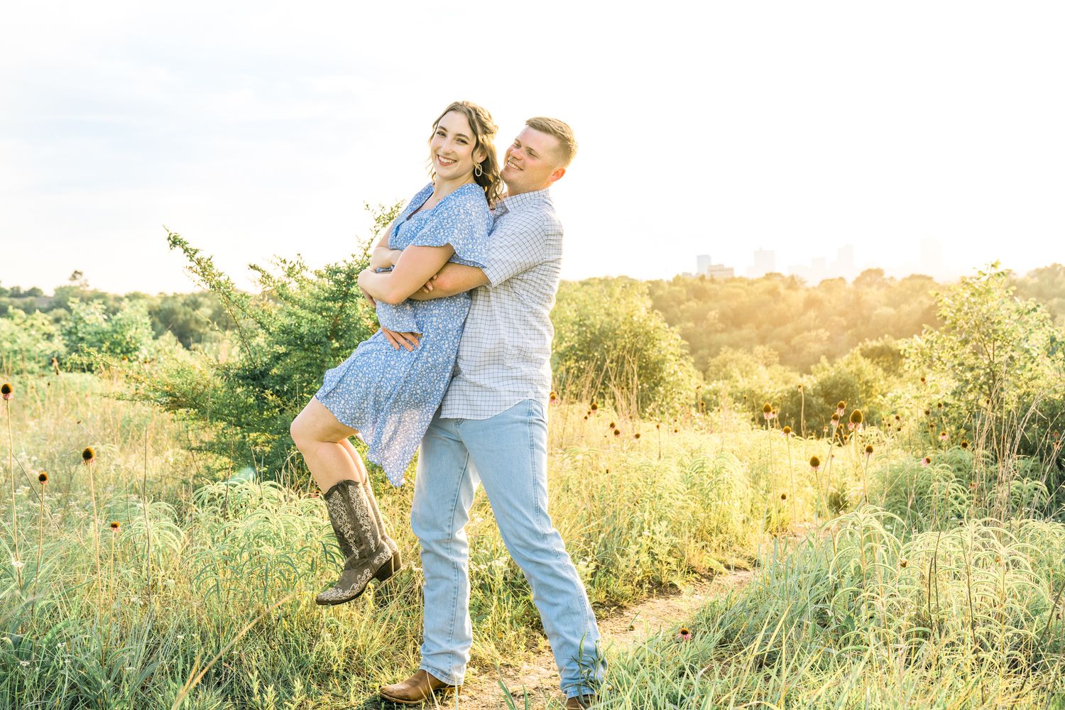Couple embraces in a golden sunlit meadow during a romantic sunset photoshoot.
