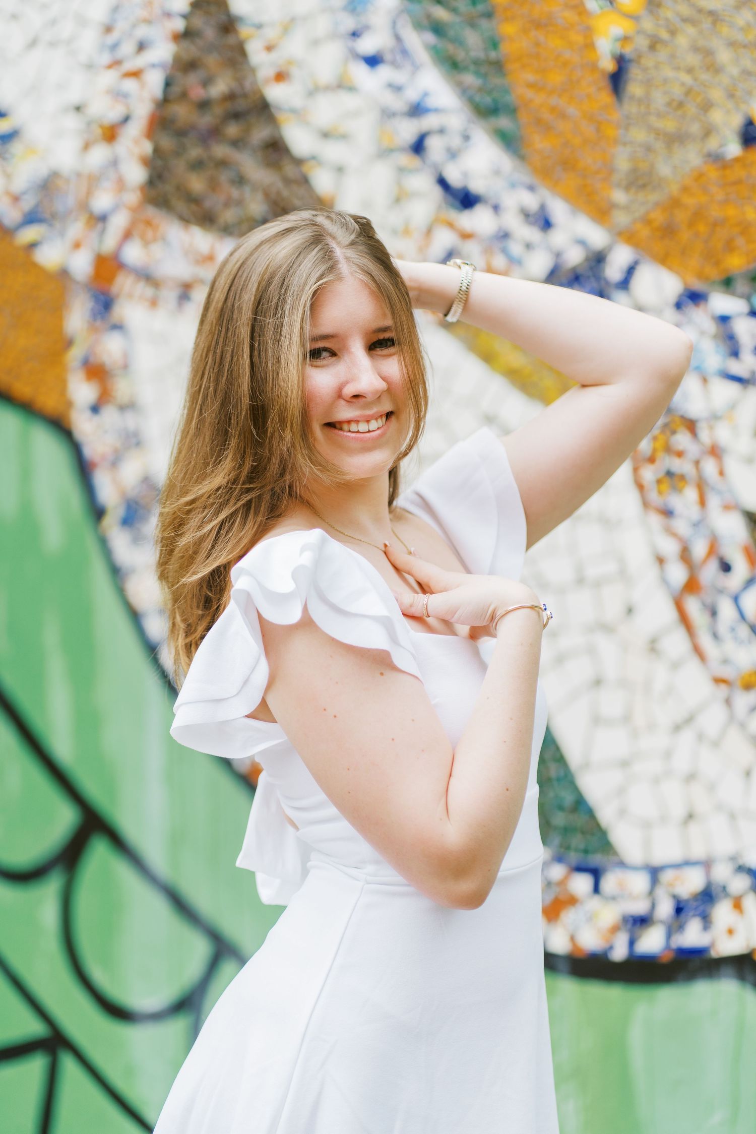 Person in white ruffled dress poses playfully against colorful graffiti wall background.