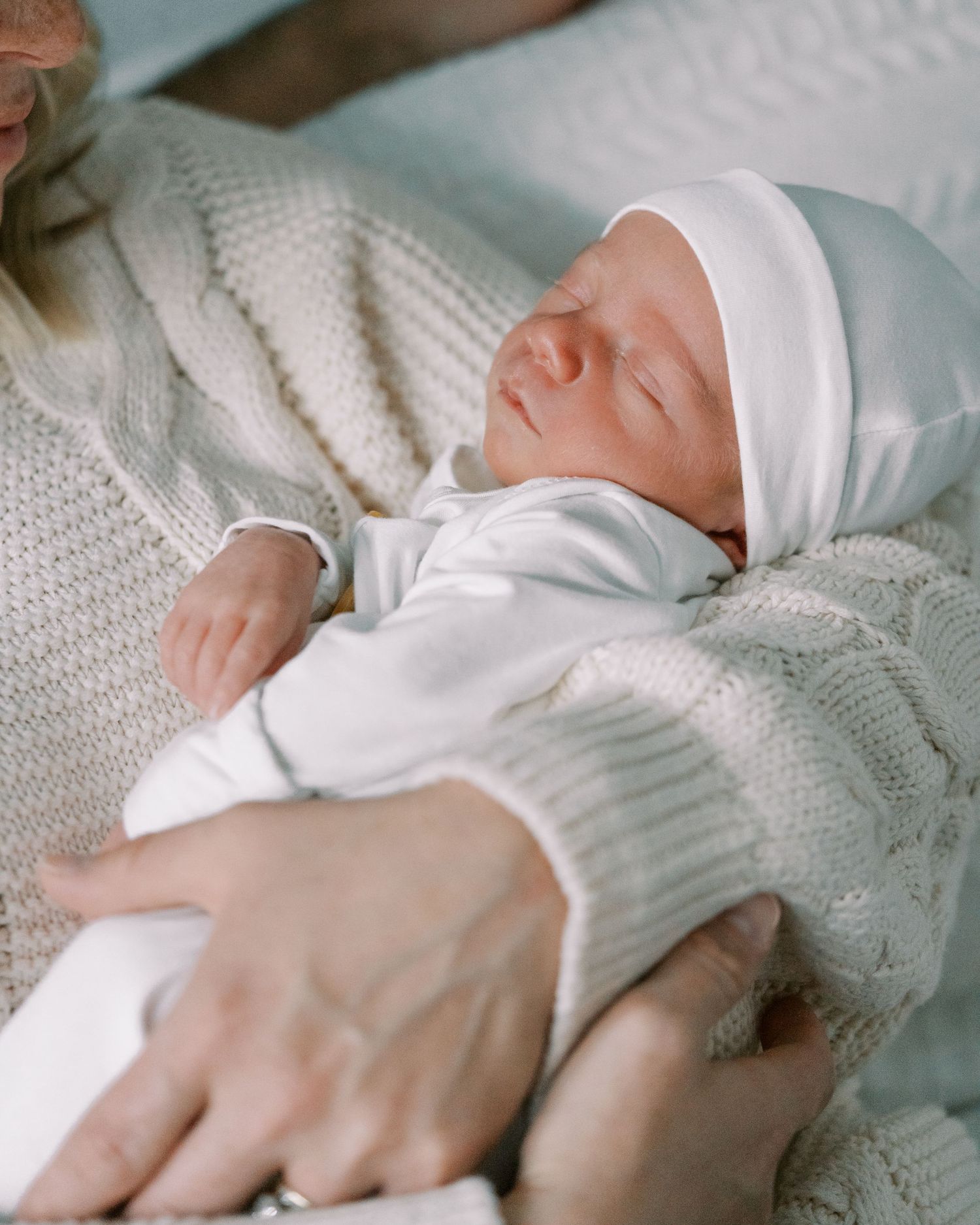 Gentle hands cradling sleeping newborn wrapped in white blanket.