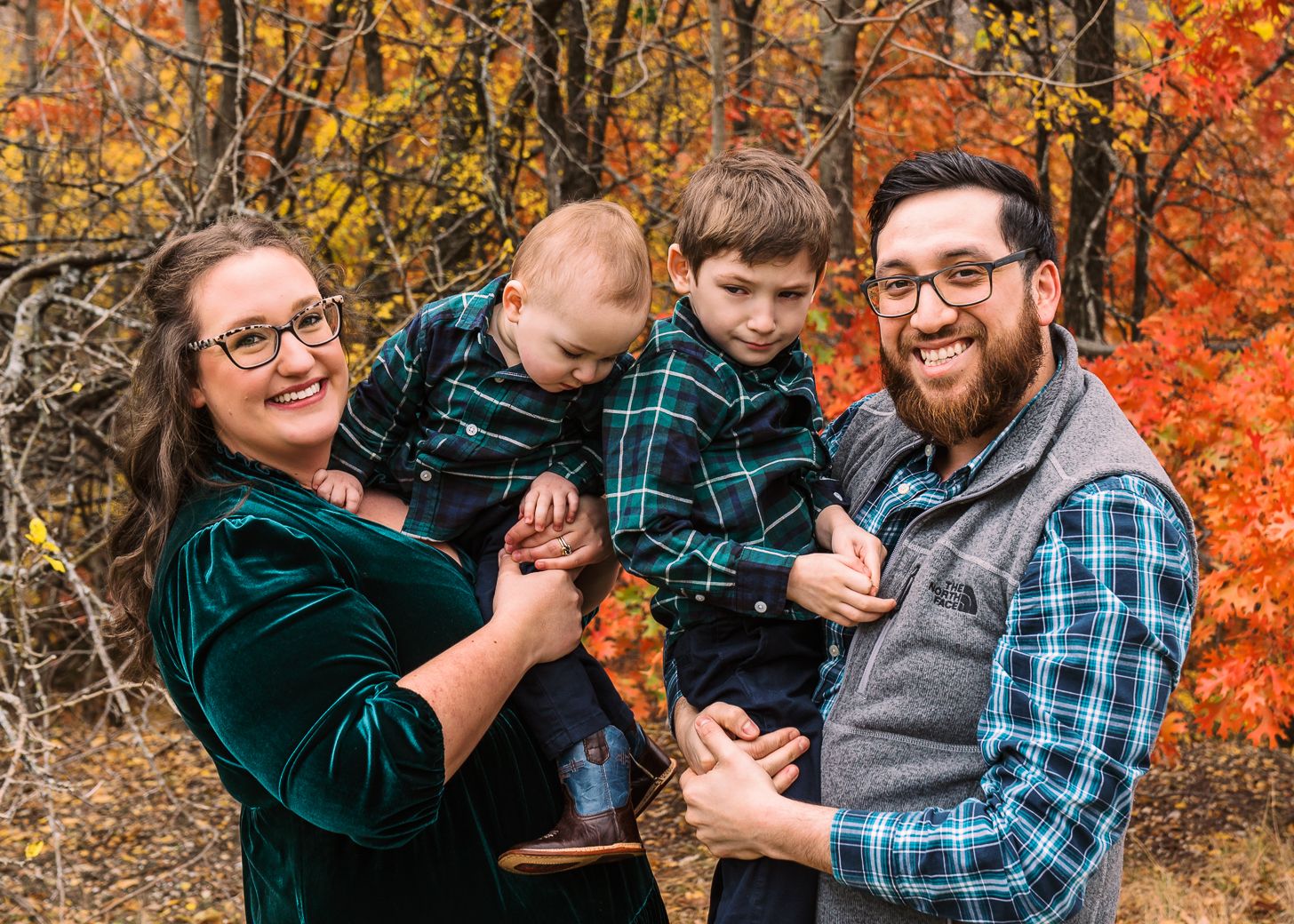 A family poses together outdoors during autumn with vibrant orange fall foliage in the background.