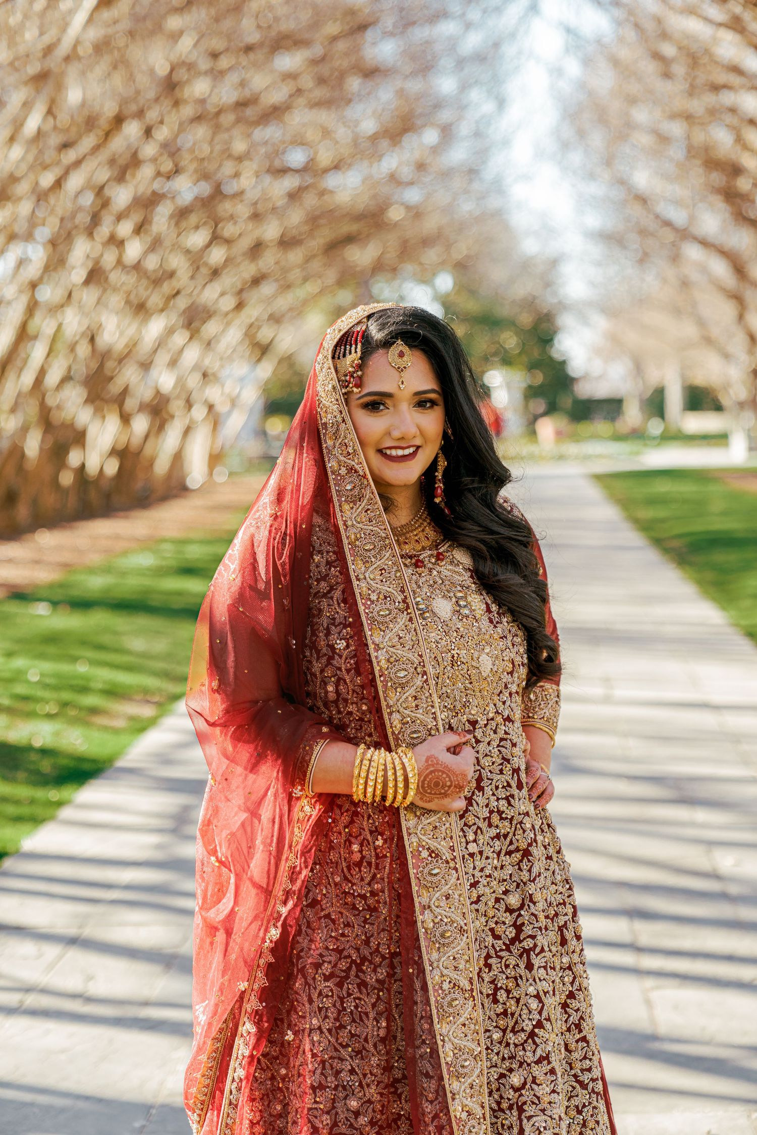 A series of photos showing a bride in an ornate red and gold traditional South Asian wedding dress walking outdoors.