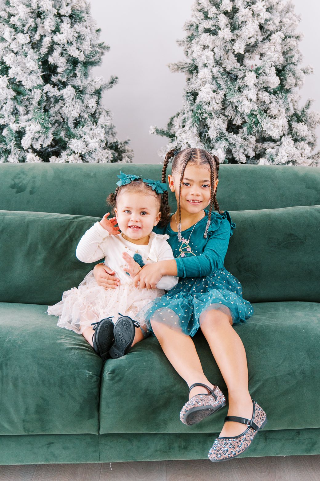Children lounging on emerald velvet sofa with flocked Christmas trees behind them.