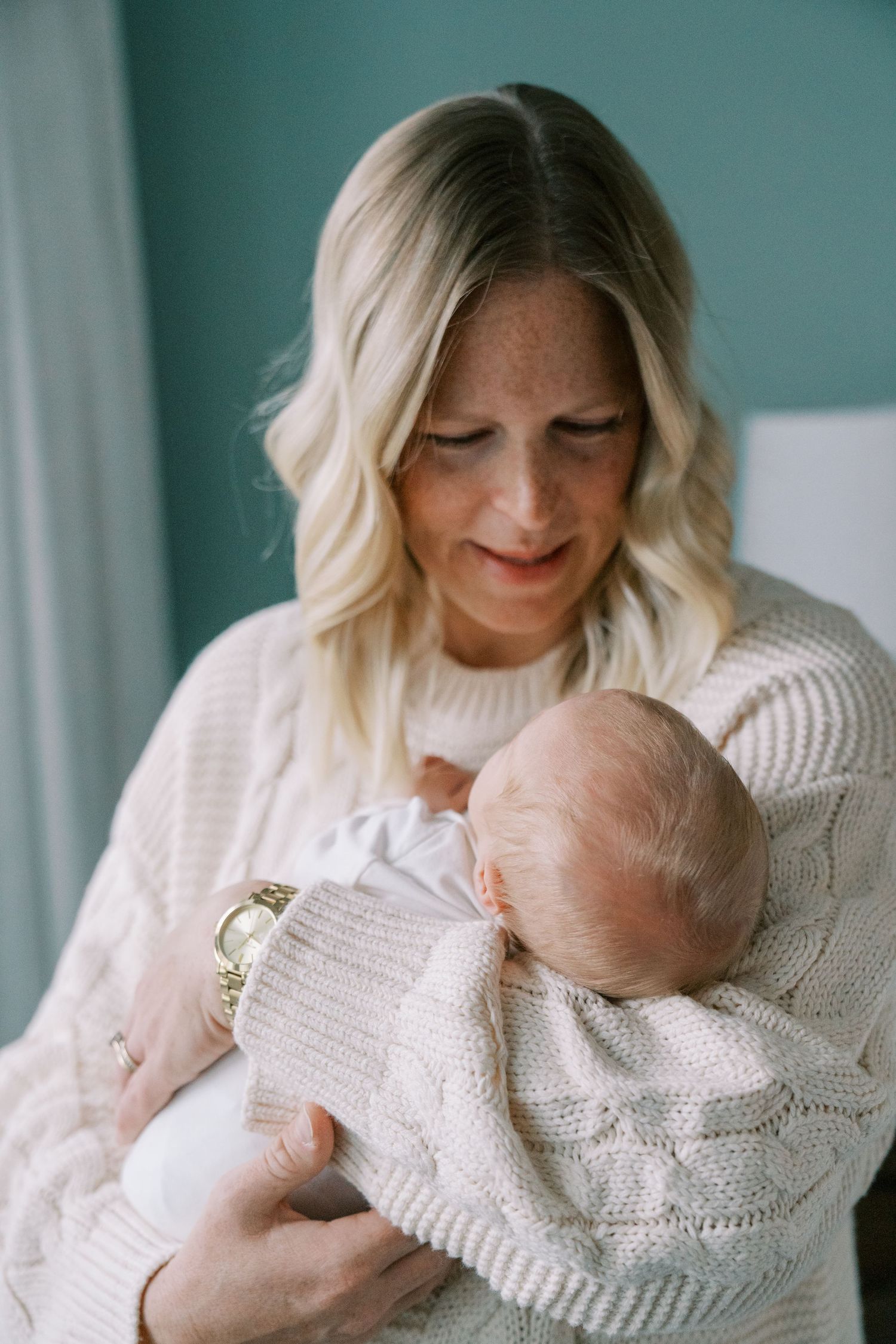Intimate portrait of mother holding newborn baby in white knit sweater.
