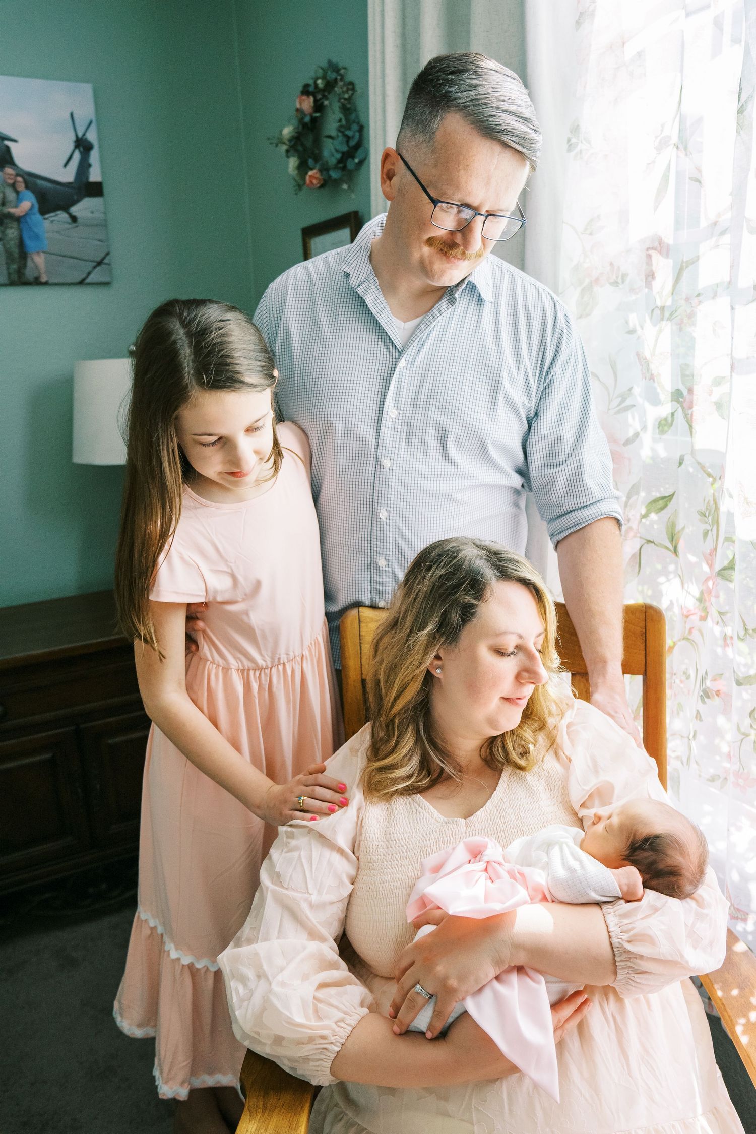 Family gathering in a mint green room sharing special moments with their newborn.