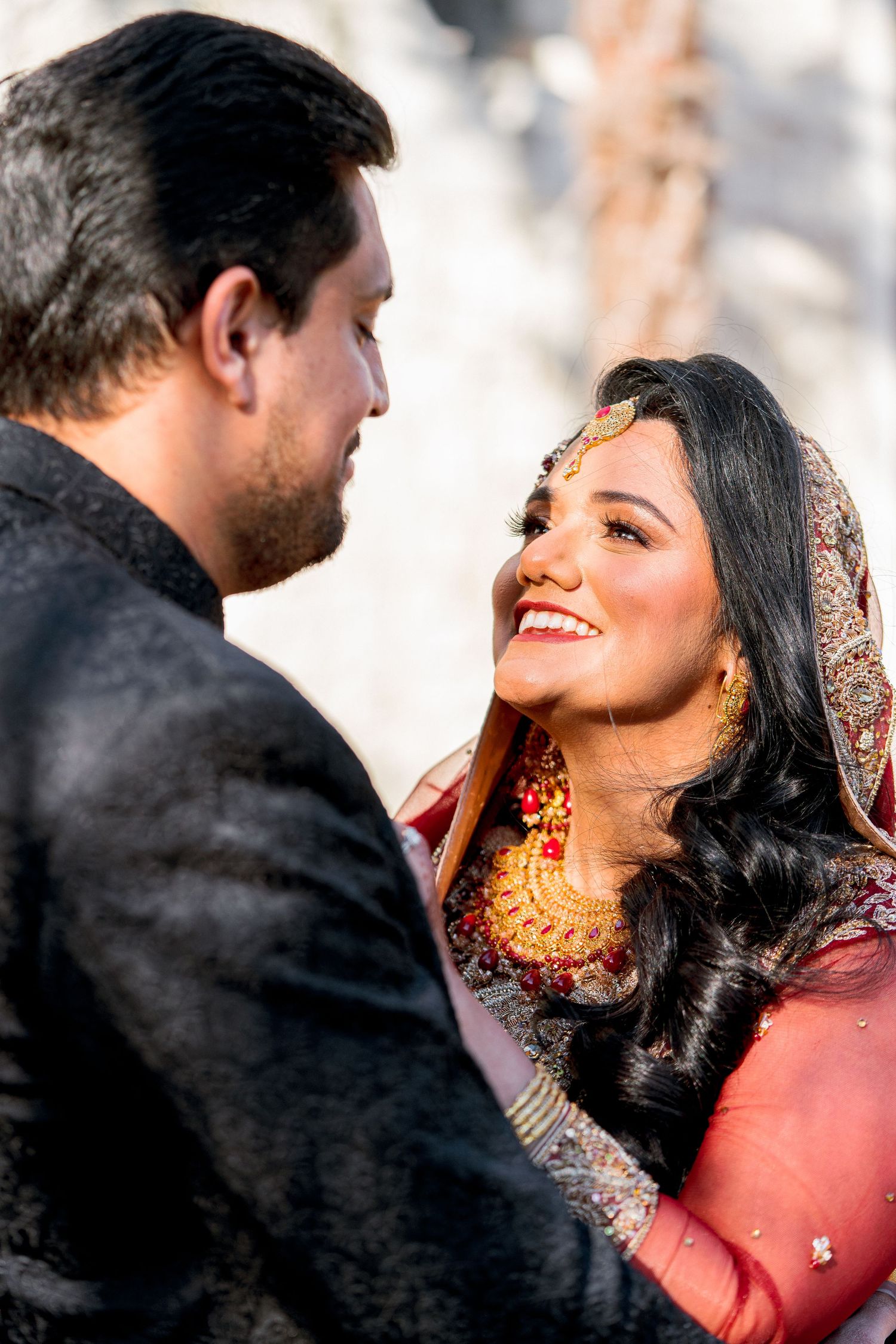 A romantic moment between a couple in traditional South Asian wedding attire, sharing a joyful glance.