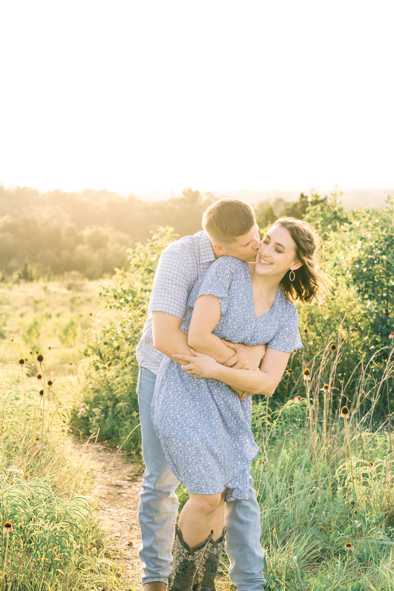 A couple embraces in a sun-drenched meadow with wildflowers and tall grass during golden hour.