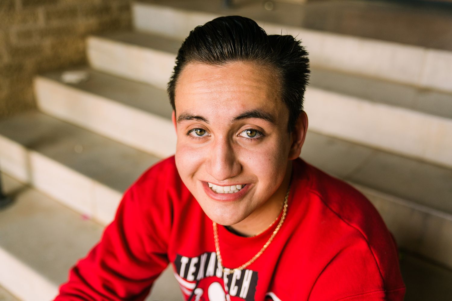 A person in a bright red sweatshirt poses in a brick archway hallway.