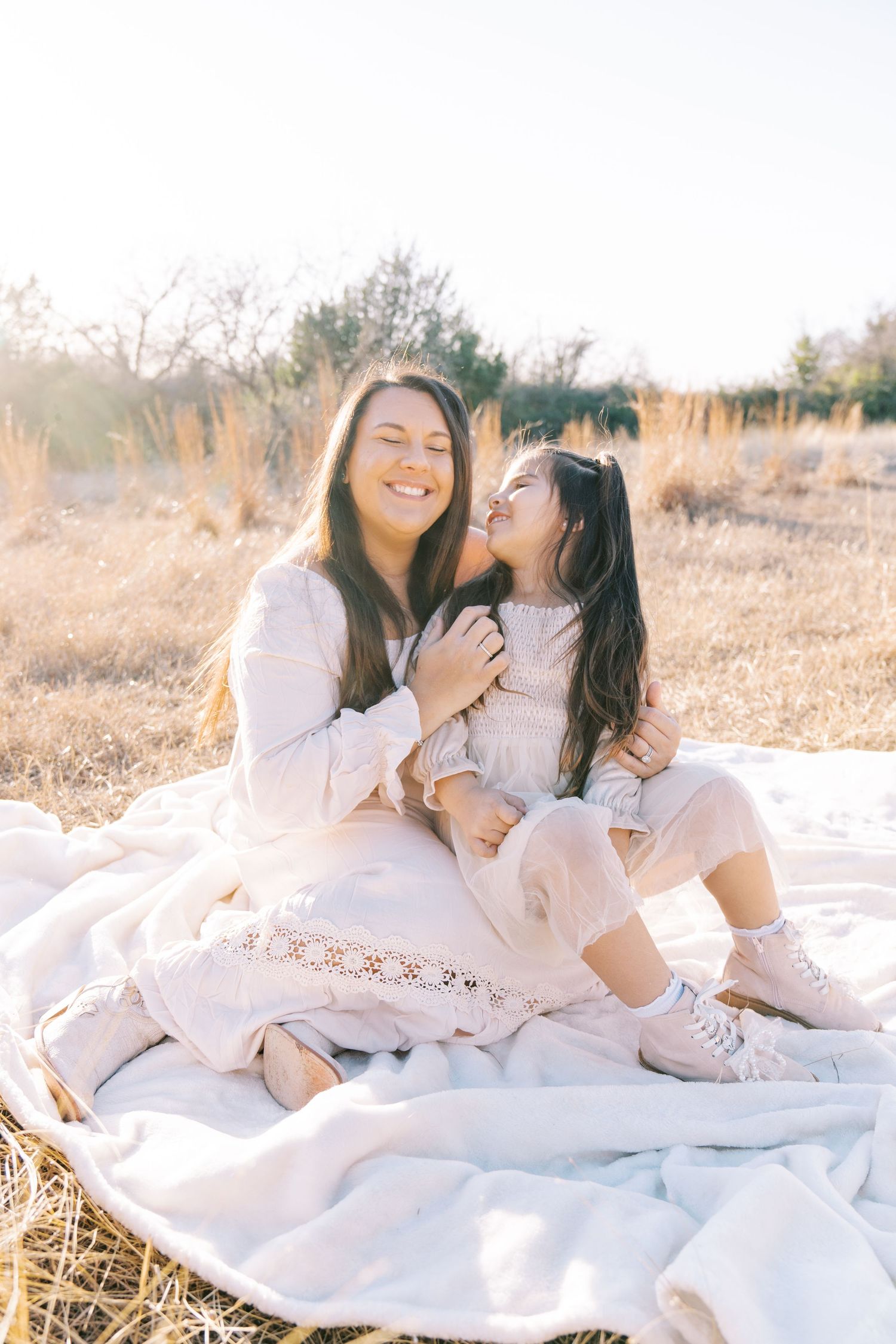 Family lying on white blanket shares joyful moments in sunny field.