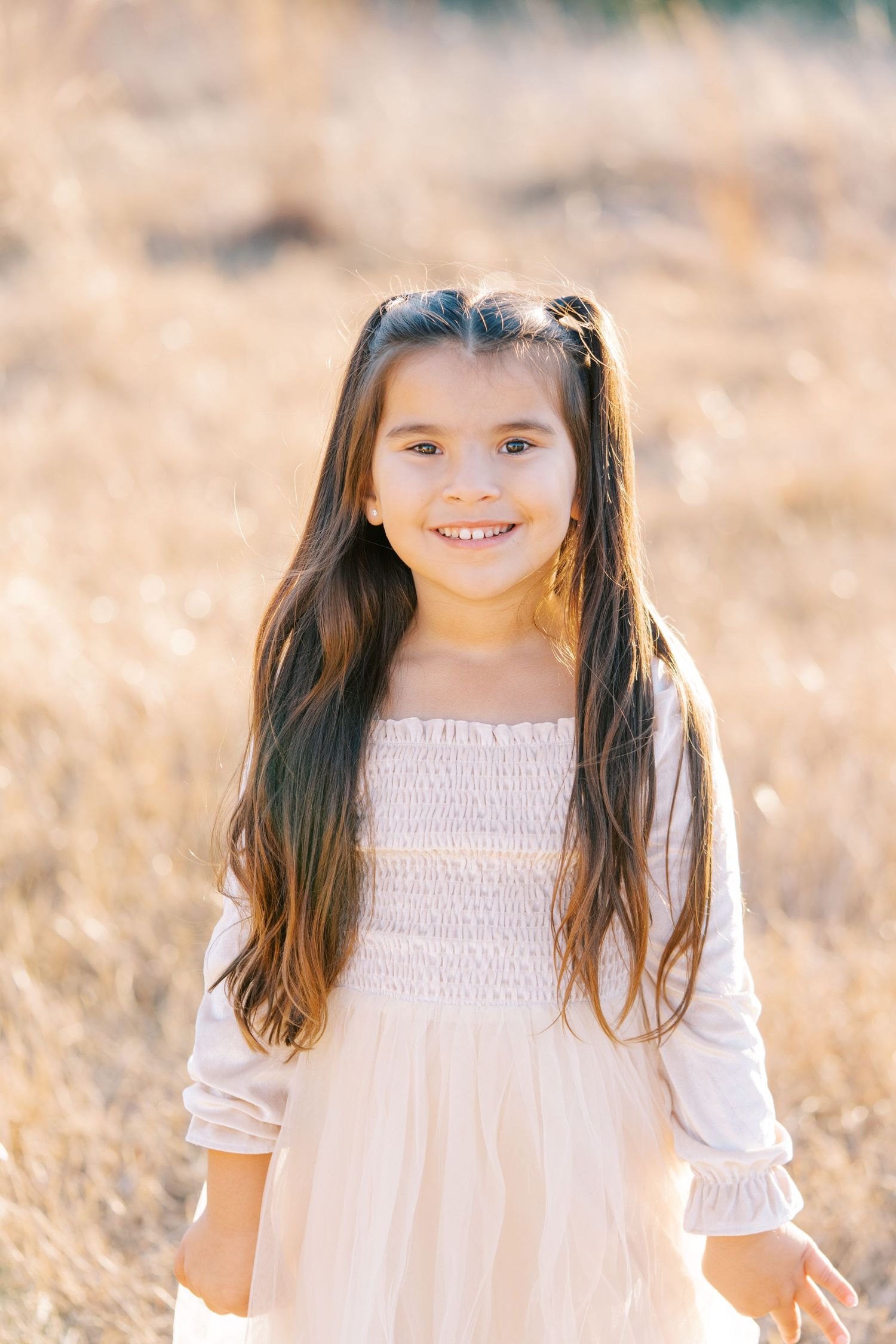 A child wearing a white smocked dress poses outdoors in golden sunlight during a portrait session.