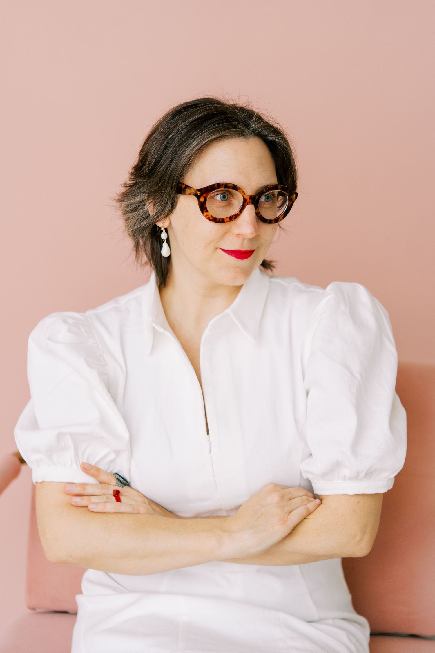 Professional portrait against pink background wearing white puff sleeve dress and tortoise shell glasses.