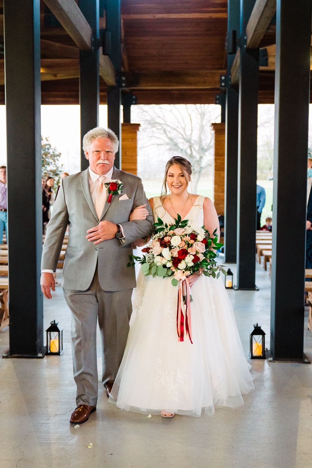 Wedding party members in gray suits and white dresses walk through a covered venue space with black columns.
