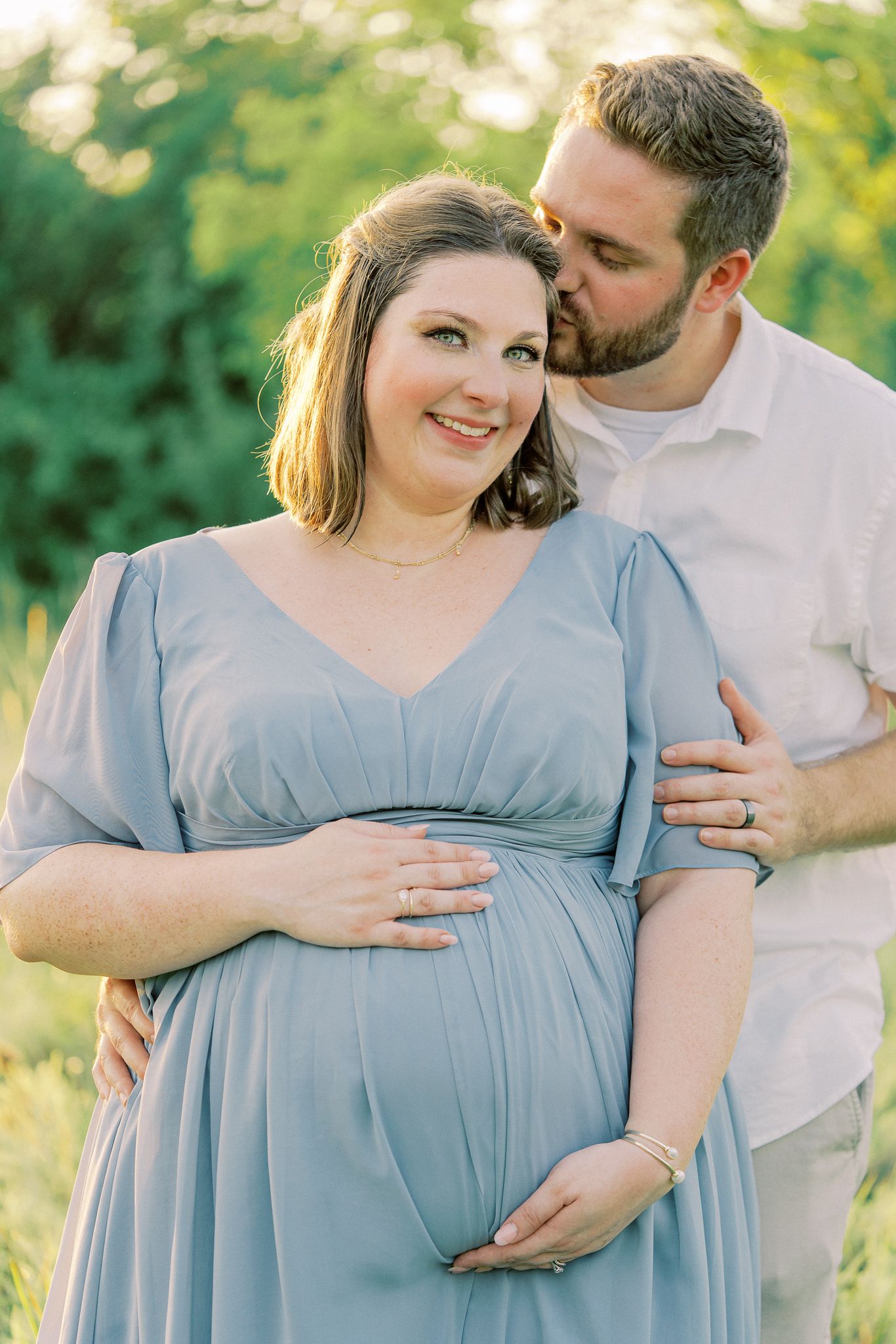 Intimate maternity photos captured in golden hour light with couple in blue dress and white shirt.