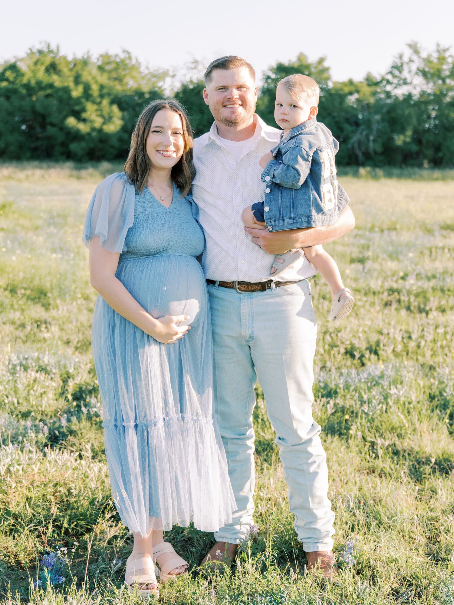 Family in coordinating blue and white outfits posing together in a sunny meadow.